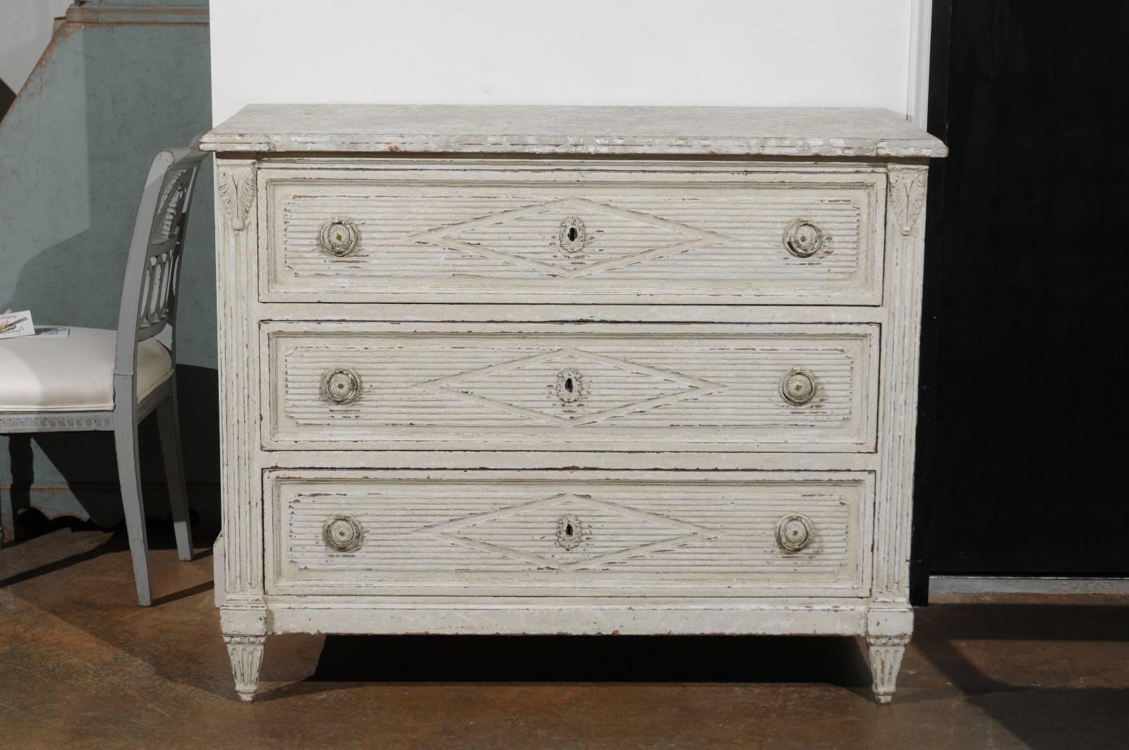 A late 18th century Danish neoclassical three-drawer commode with reeded decor and diamond motifs. Born in Denmark during the later years of the 18th century, this painted wood commode features a rectangular top with slightly protruding corners
