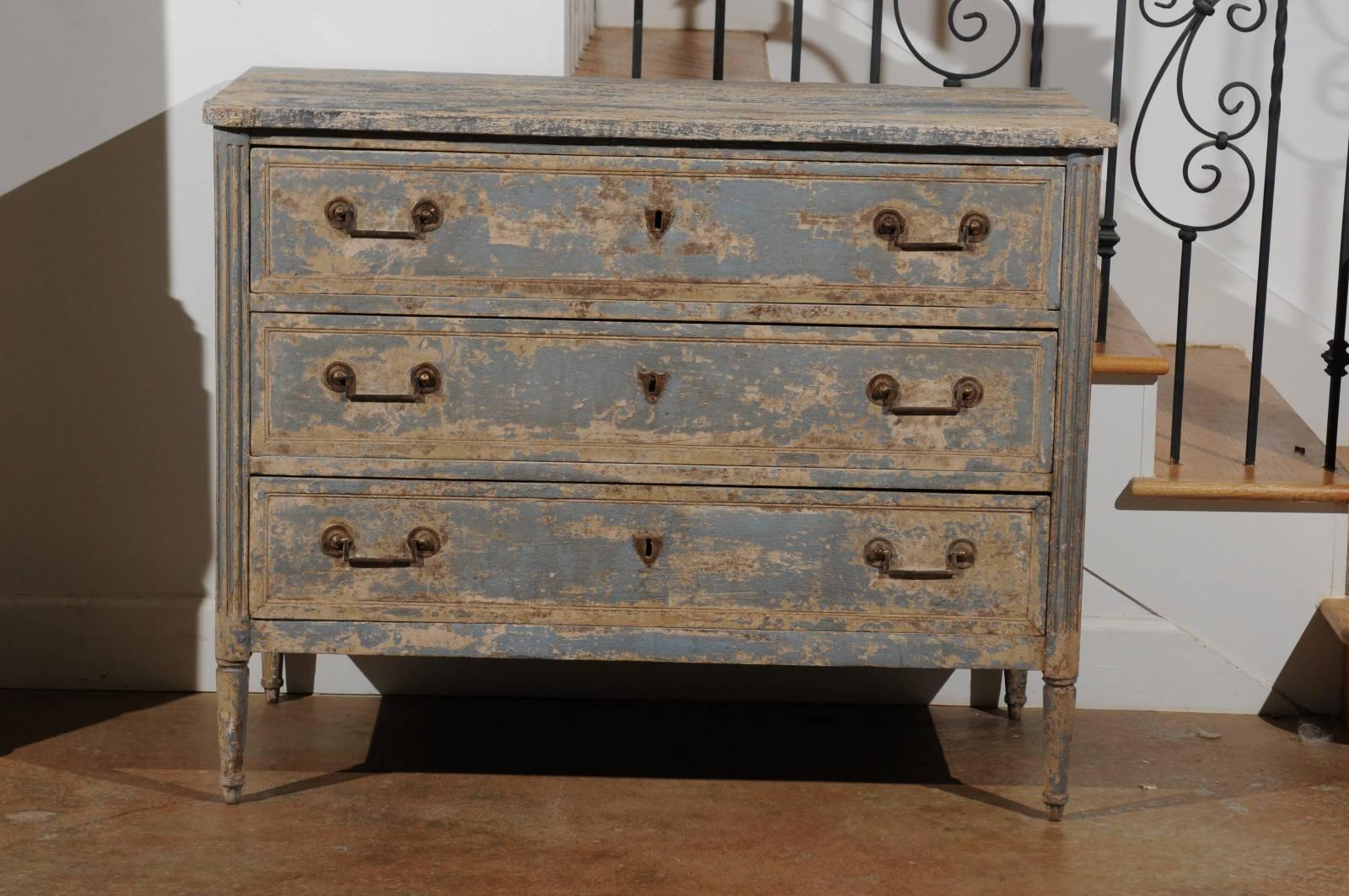 A Swedish Gustavian period blue painted three-drawer commode with fluted side posts and cylindrical feet from the early 19th century. This Scandinavian chest-of-drawers features a rectangular top with rounded corners in the front, sitting above