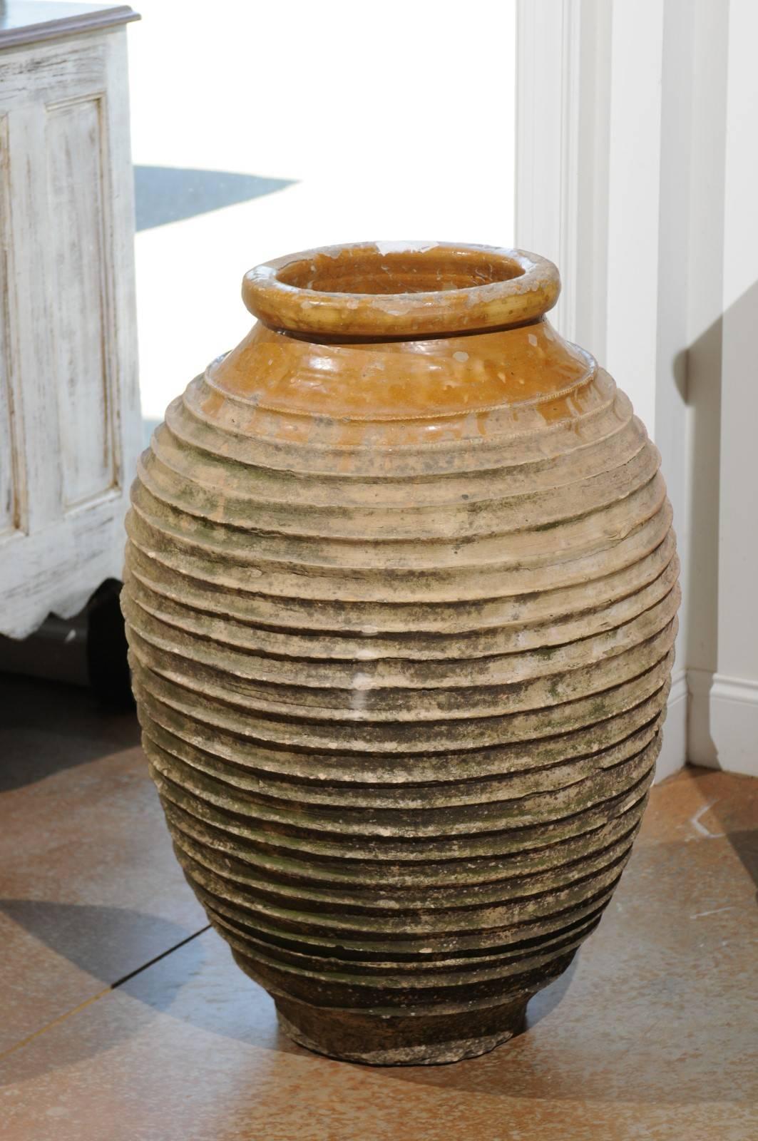 An early 19th century Greek medium size terracotta ribbed olive jar with traces of glaze in the upper section. This olive terracotta jar was born in Greece in the early 1800, where it was used to store olive oil. It features a typically Greek style