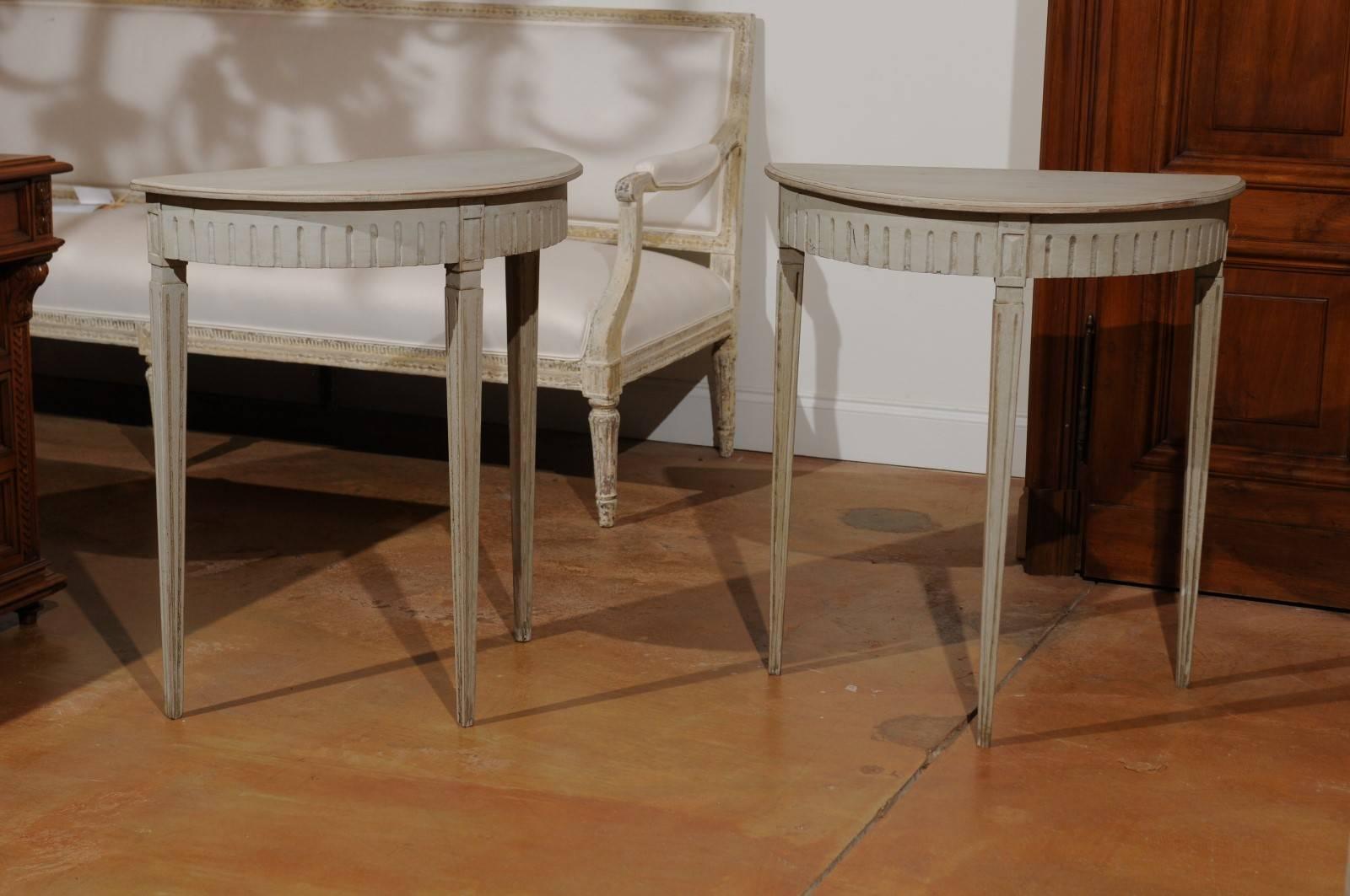 A pair of Swedish neoclassical style painted wood demilune console tables with tapered legs from the 19th century. Each of this pair of Swedish demilunes features a semi-circular top sitting above a fluted apron. Each table is raised on slender