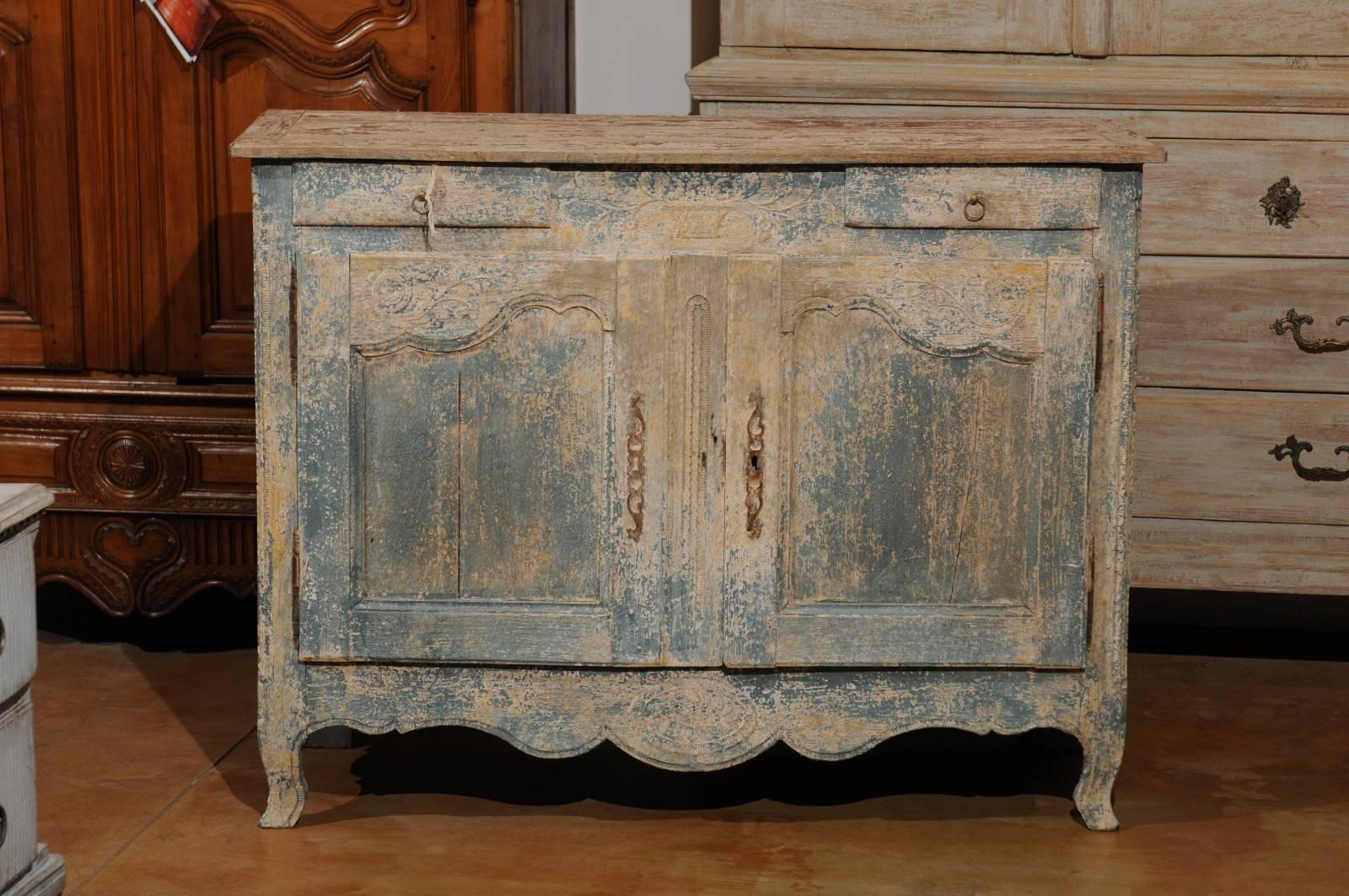 A French Louis XV style painted wood two-door, two-drawer buffet with floral motifs and distressed finish from the early 19th century. Born in the early years of the 19th century, at a time when Bonaparte was about to crown himself emperor and