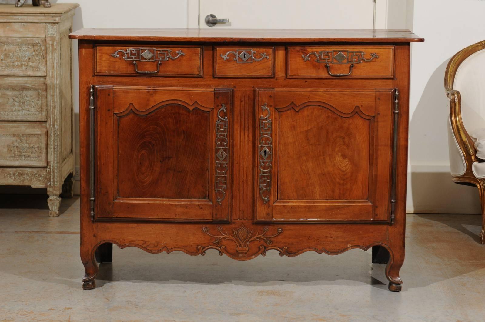 A French cherry three-drawer, two-door buffet with scalloped apron and scrolled feet from the 19th century. This French buffet features a rectangular top with rounded corners in the front, overhanging three drawers, a smaller one flanked with two