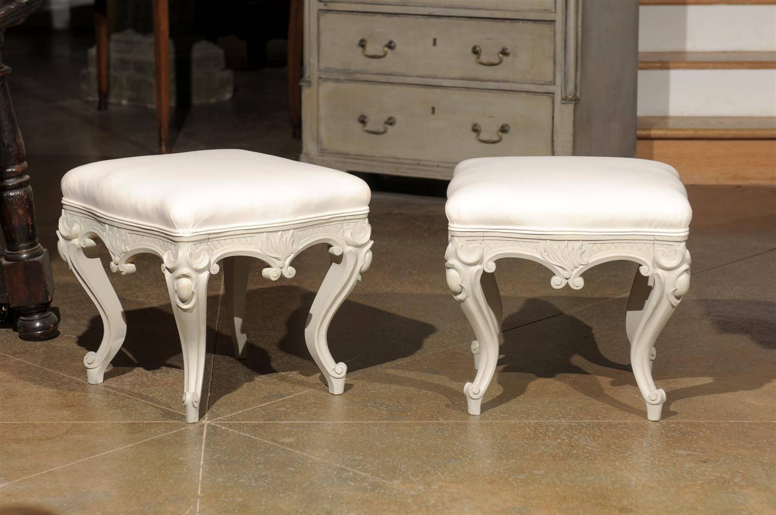 A pair of Swedish Rococo style painted stools from the late 19th century with richly carved décor, cabriole legs and newly upholstered seats. Each of this pair of Scandinavian Rococo style stools features a square seat reupholstered in a double welt