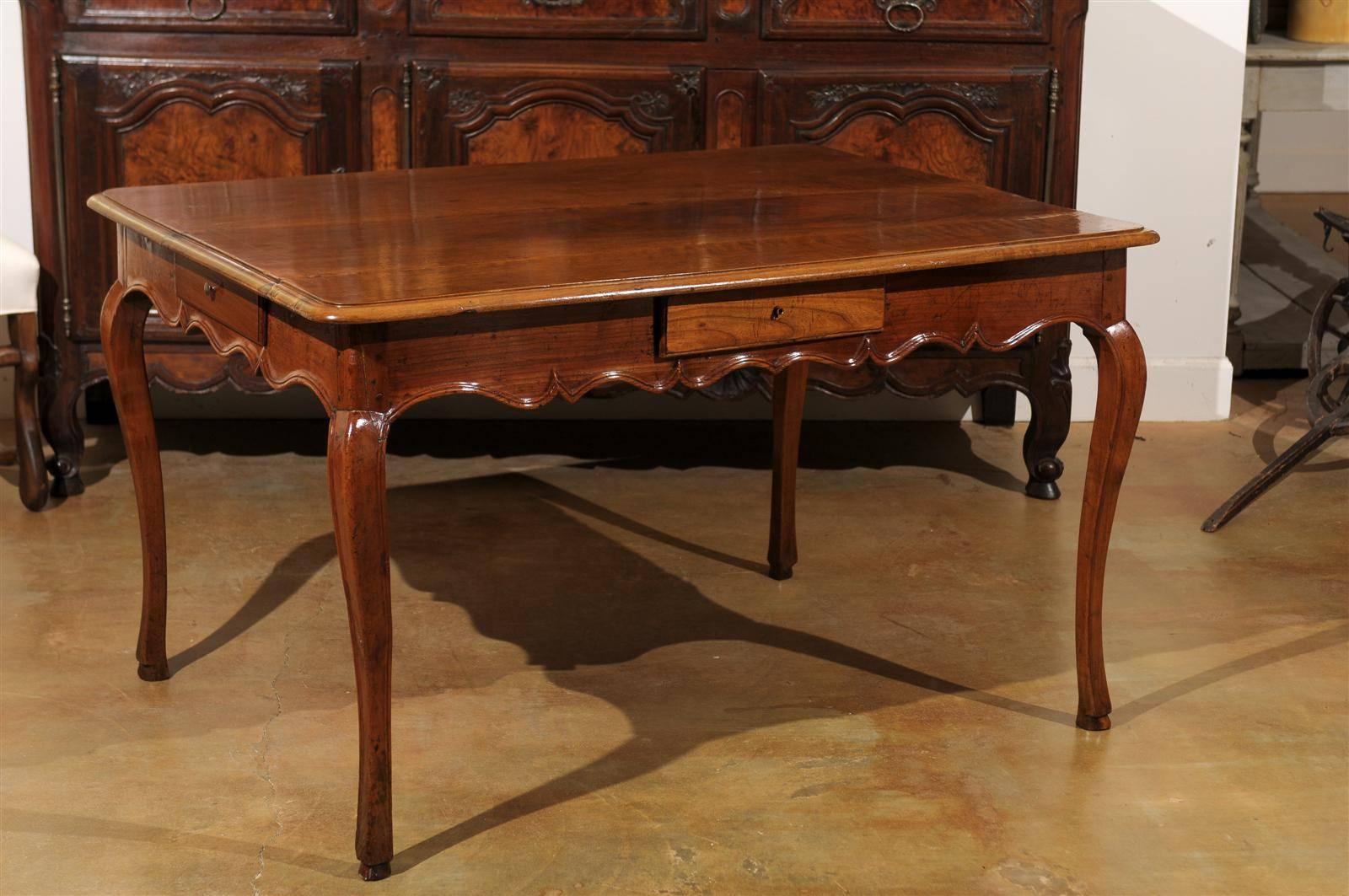 A French Louis XV style walnut four-drawer table with cabriole legs from the mid 19th century. This walnut table features a rectangular top with rounded edges, overhanging an apron comprising a drawer on each side. This apron is scalloped on all