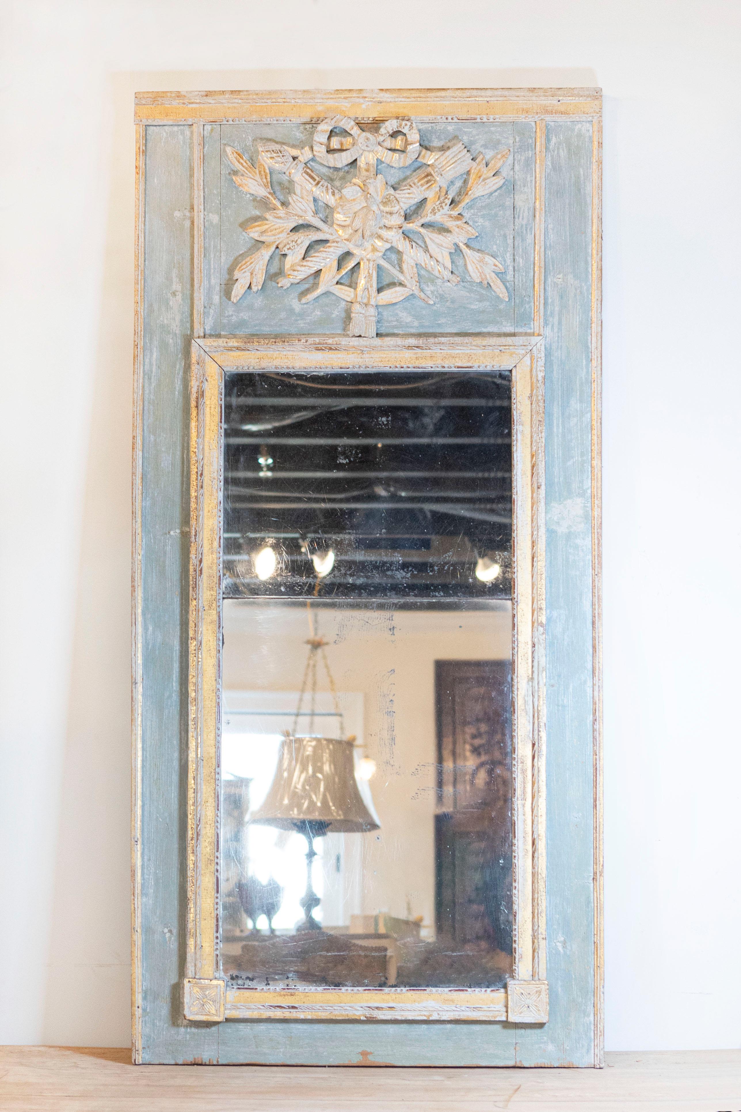A French Louis XVI period green painted and parcel gilt trumeau mirror from the 18th century with carved trophy. Step into the Classical elegance of the 18th century with this French Louis XVI period trumeau mirror, a piece that beautifully