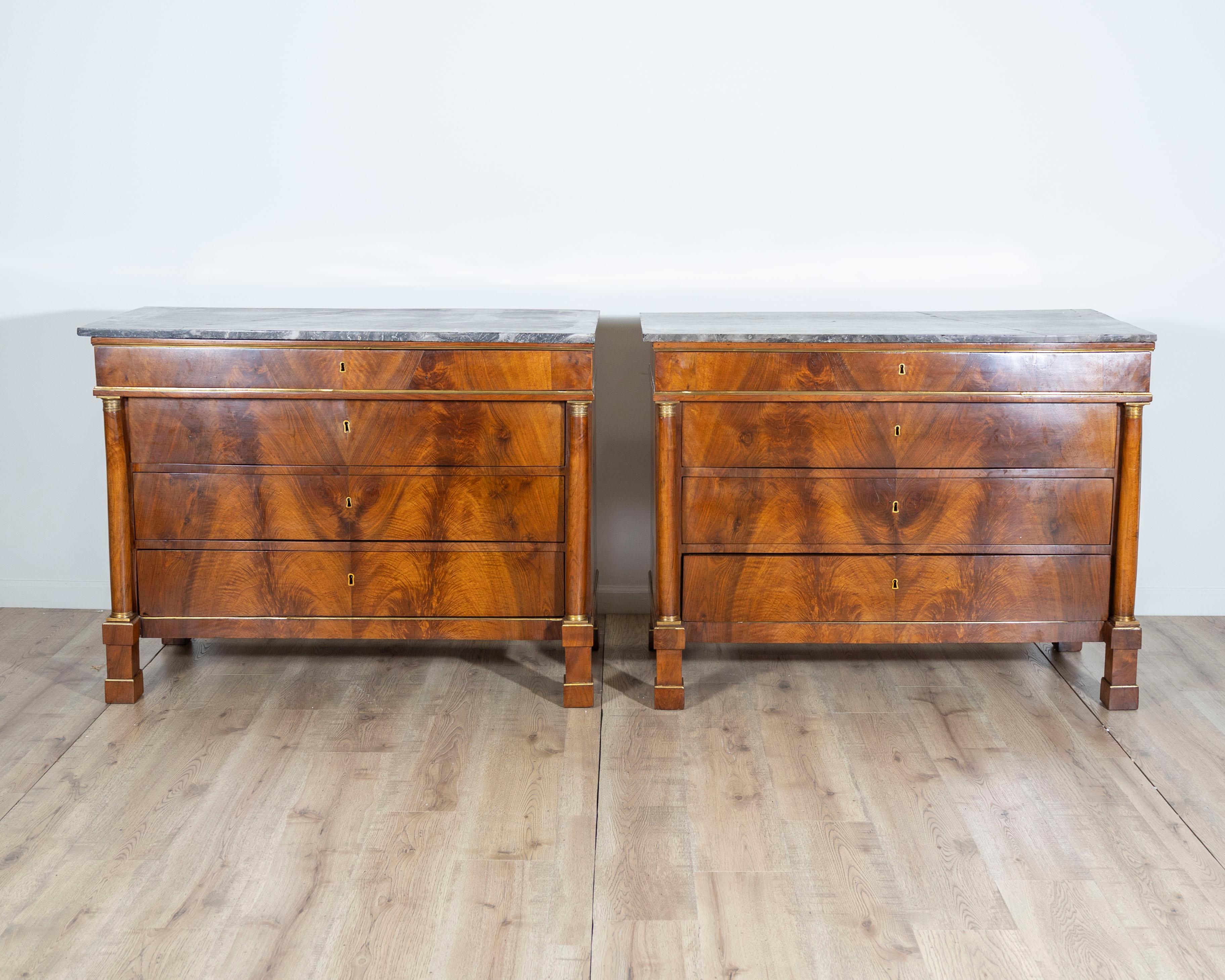 This elegant pair of Italian commodes dates to the early 19th century and embodies the refined neoclassical style of the period. Crafted in richly figured walnut, each piece features a dark gray marble top with striking white veining, resting above