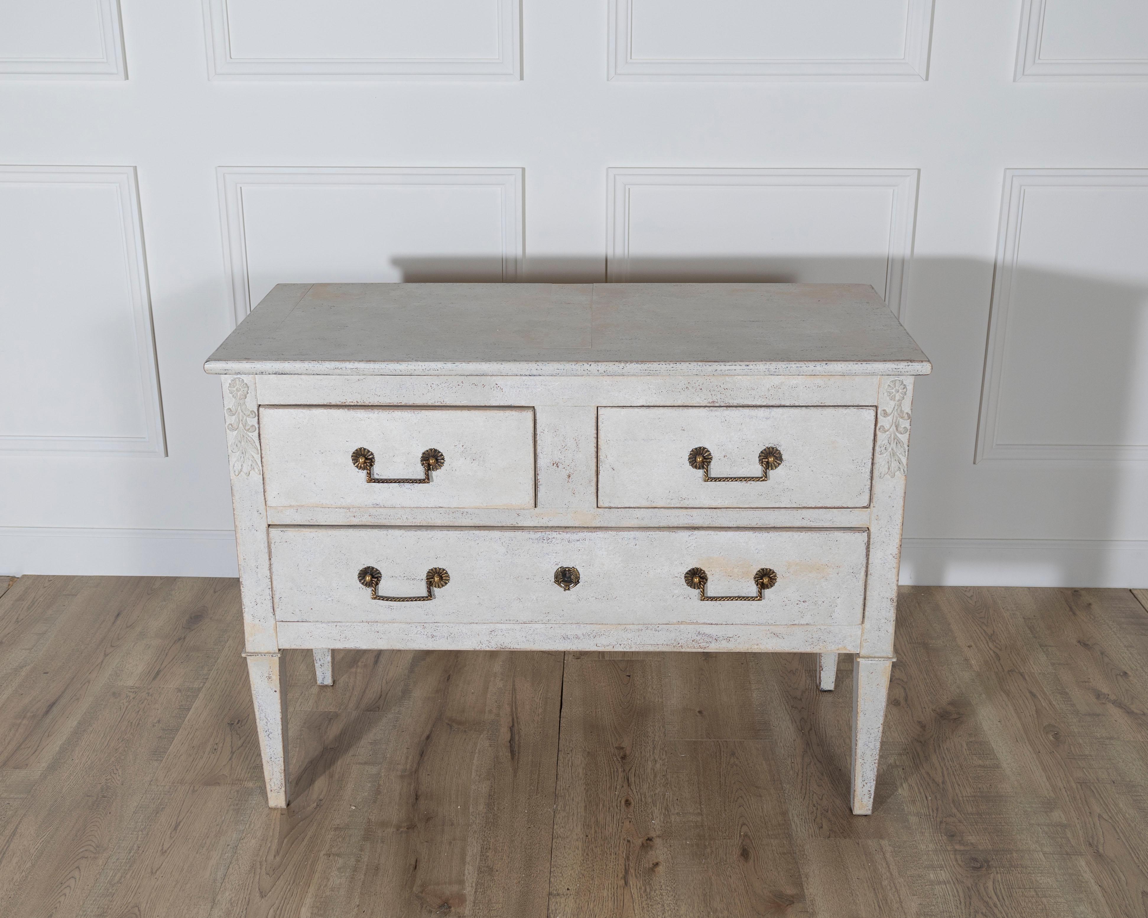 Charmante commode française datant d'environ 1920, magnifiquement peinte dans un ton sable clair qui met en valeur sa silhouette raffinée. La pièce repose sur d'élégants pieds fuselés et est ornée de discrets détails floraux sculptés juste sous le