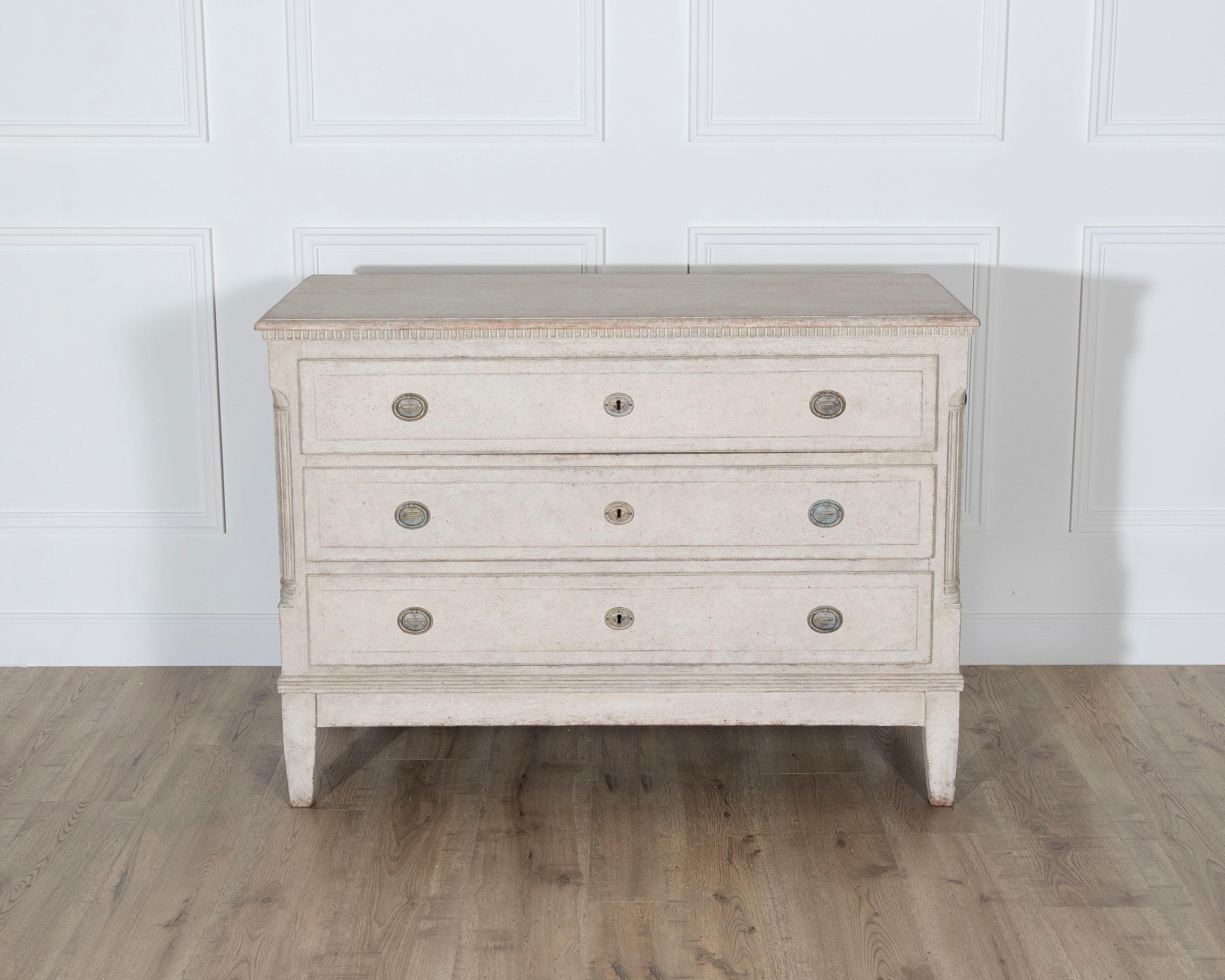 Une commode danoise ancienne magnifiquement proportionnée, fabriquée au 19ème siècle et finie dans une peinture beige douce avec une patine finement vieillie. Les trois tiroirs spacieux sont encadrés d'une délicate moulure et ornés d'écussons et de