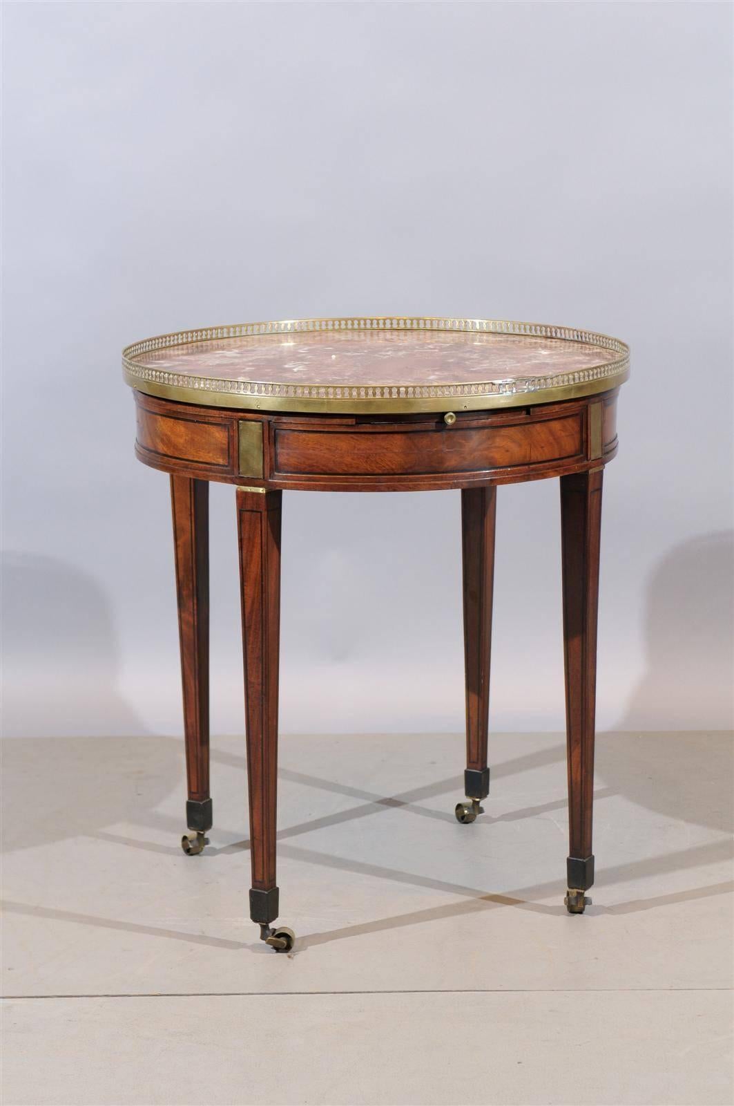 A Louis XVI style walnut bouillotte table with marble top, brass gallery and mounts, inlay and tapered legs with castors. 

