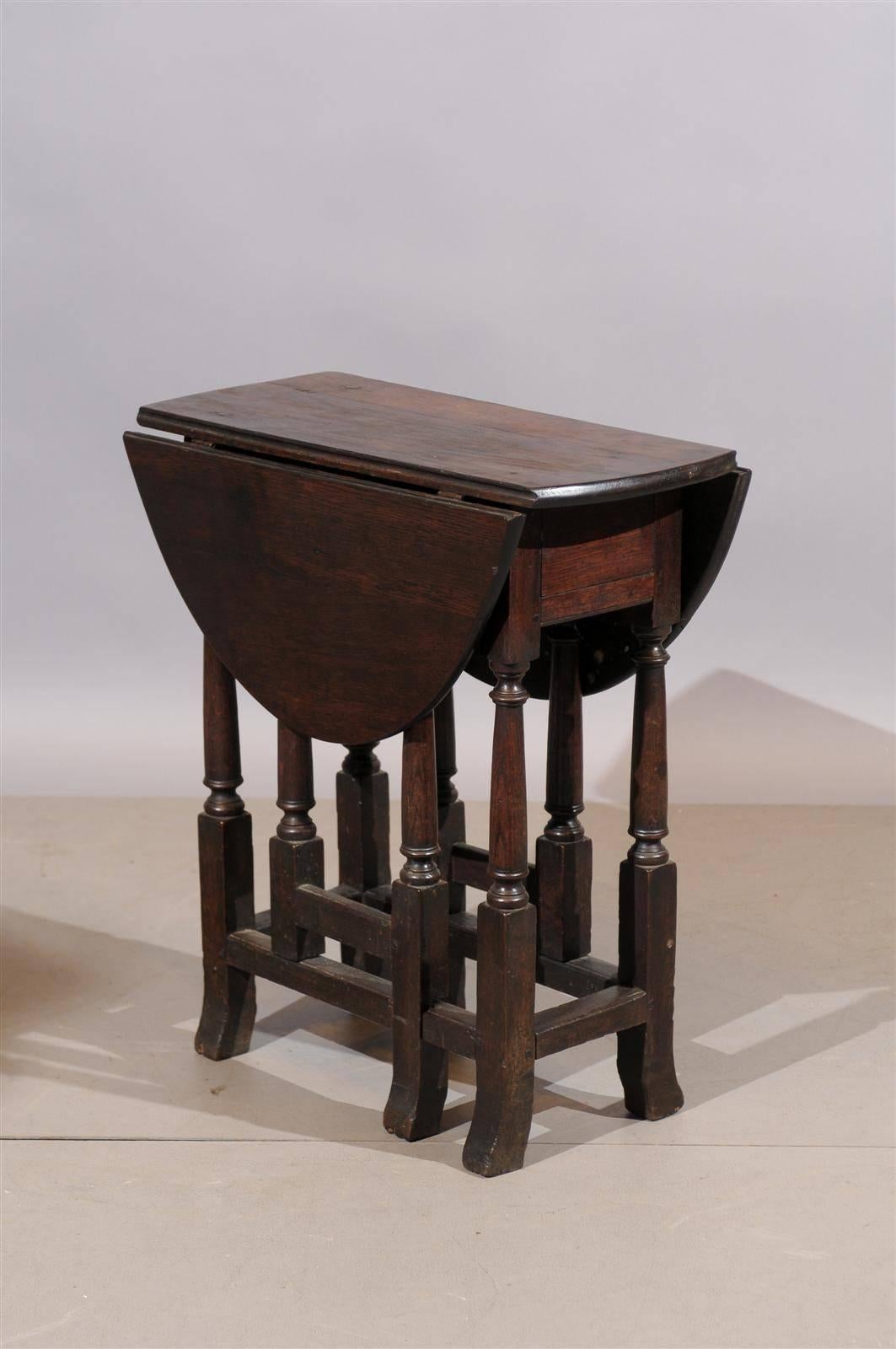 A 18th century English oak gate leg table with drop leaves, drawer, and stretcher.