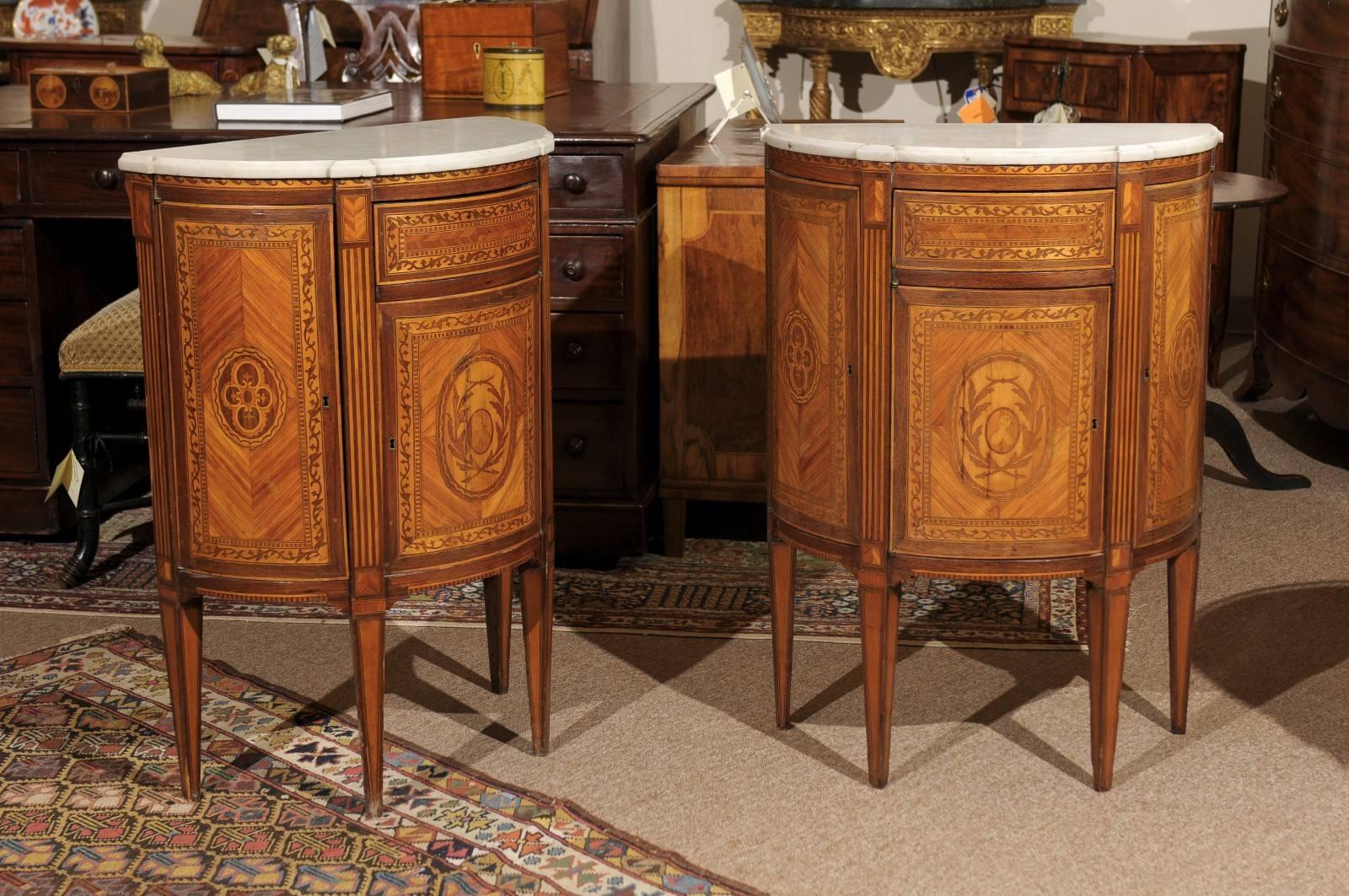 Pair of petite demilune-shaped cabinets with three doors, one drawer above the centre door and white marble tops, neoclassical style inlaid designs in kingwood, tulipwood and boxwood, Italy, circa 1940.