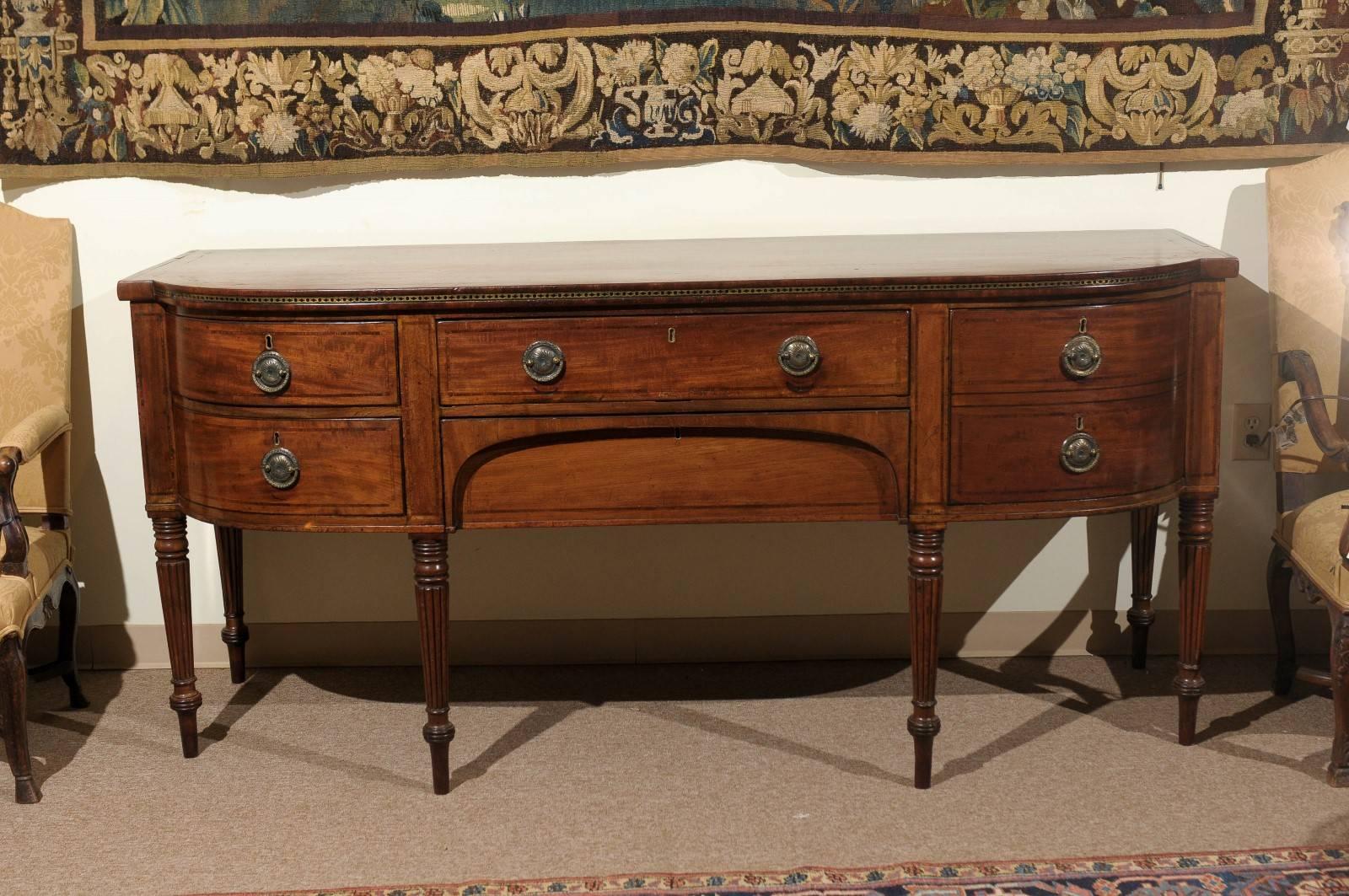 An early 19th century English bow-front Regency sideboard in mahogany with brass inlay and turned reeded legs. 

 