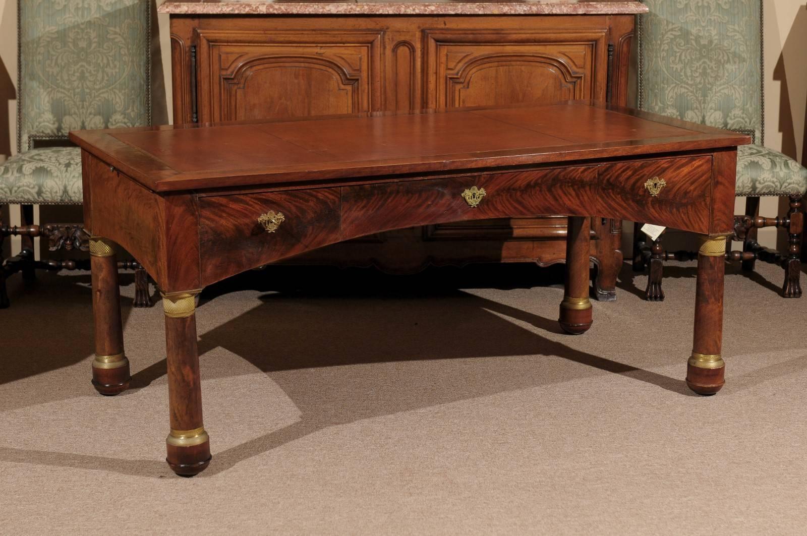 Large Empire French writing desk or bureau plat with embossed brown leather top, bronze dore mounts, column legs, and  three drawers.