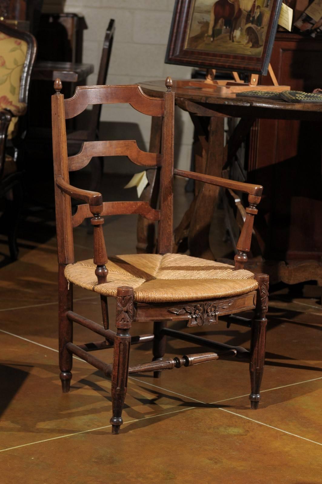 Mid-19th Century Louis XVI style walnut arm chair with ladder back, rush seat, fluted legs, and carved apron.