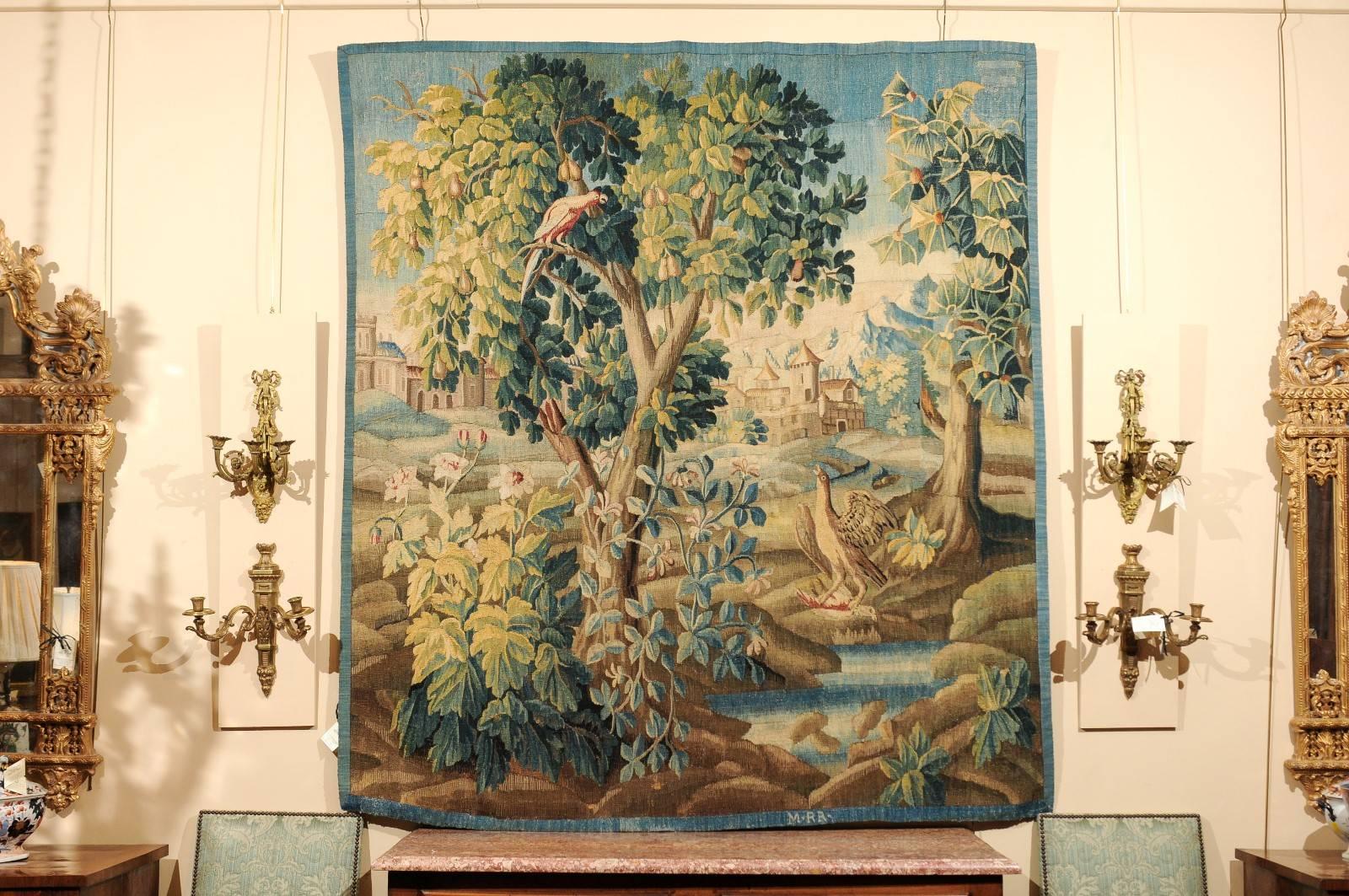 French 18th century verdure tapestry featuring a village through trees with birds. In blues, greens and earth tones.



 