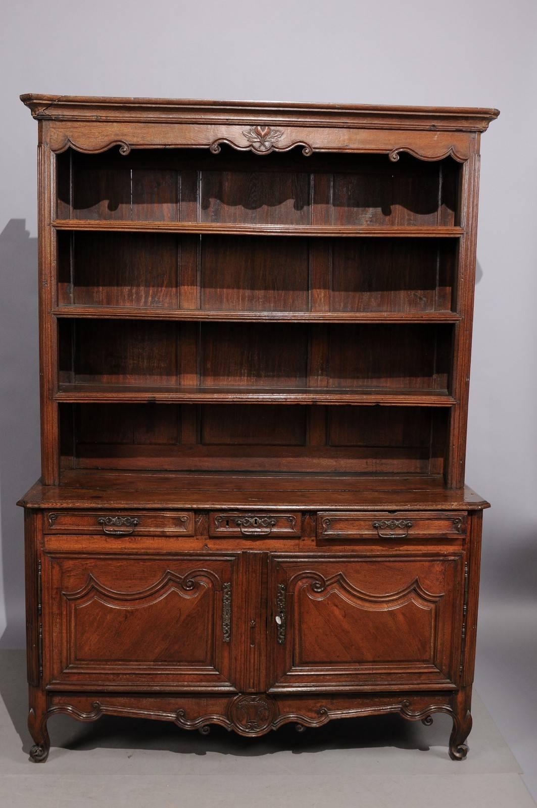 A 18th century French Transitional Louis XV & Louis XVI vaisellier in oak featuring plate shelving above buffet cabinet with 3 drawers, 2 carved paneled doors and shaped apron ending in cabriole legs. 

 