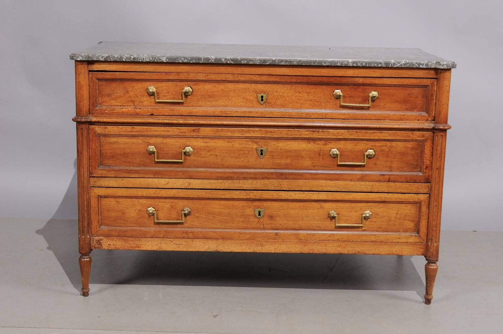Late 18th century French walnut commode with grey marble top, three drawers, brass pulls, fluting and turned tapered legs. 

 