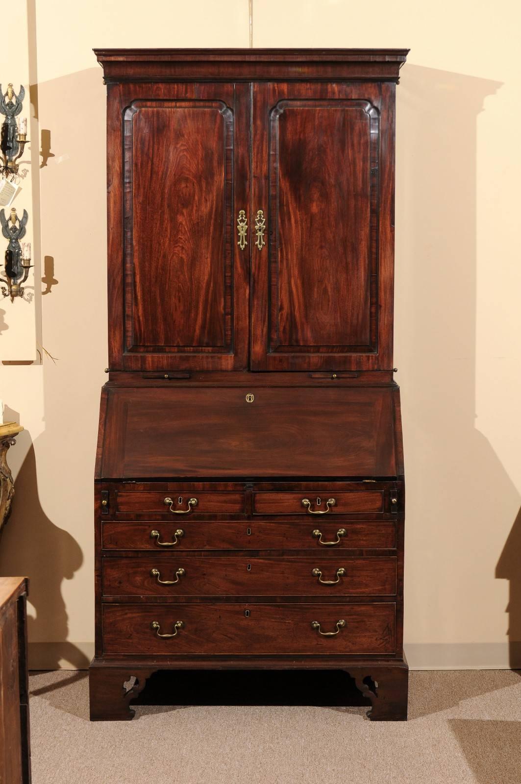A mid-18th century George II mahogany bureau bookcase with blind panel doors, slant front and bracket feet. The drop front reveals serpentine shaped cubby holes and leather writing surface.
  