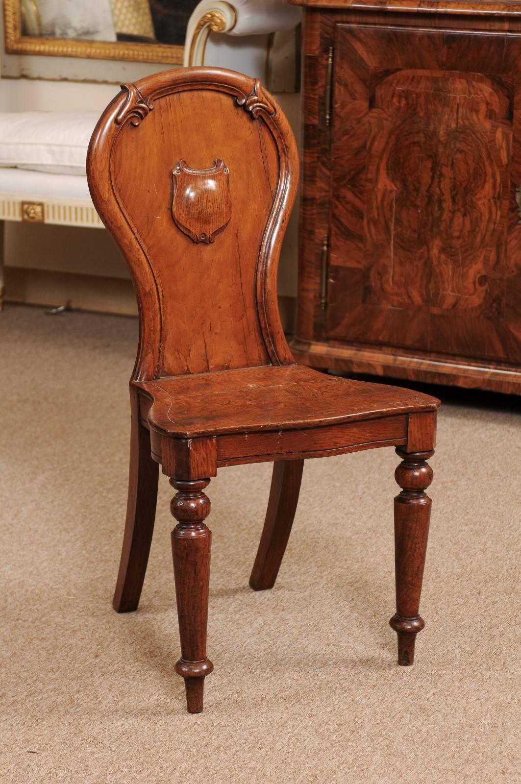 Oak hall chair featuring crest carving with turned front legs and splayed rear legs, England, Late 19th century.