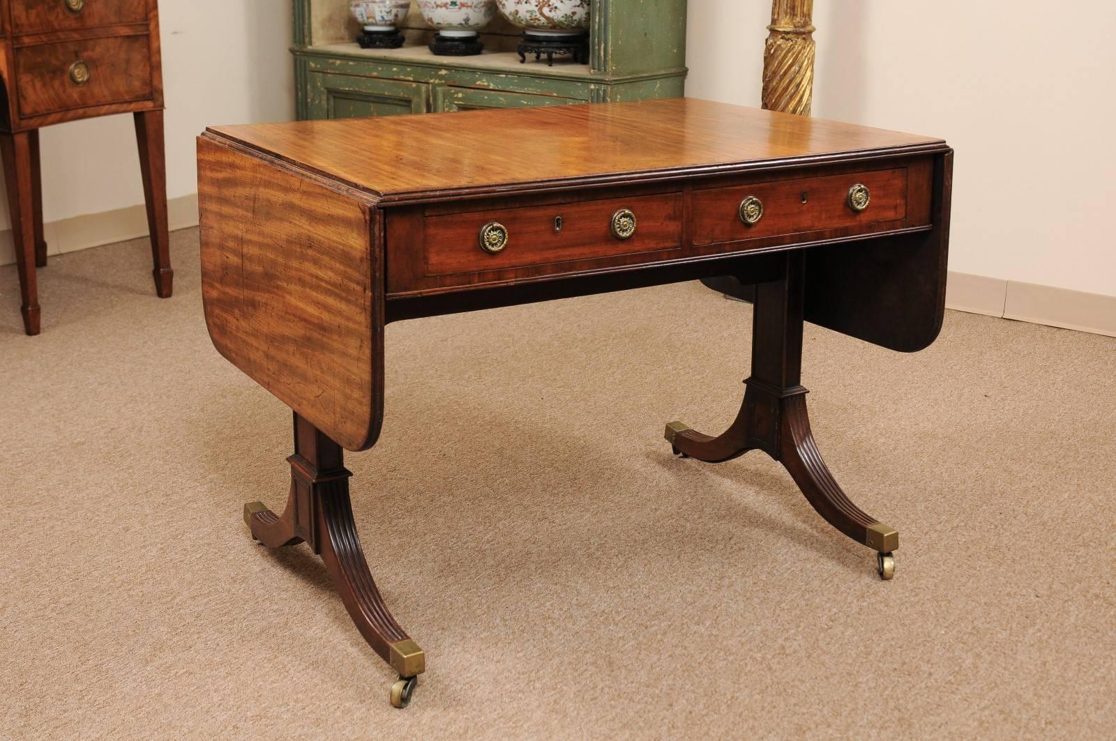 An early 19th century English Regency mahogany sofa table with reeded edge, 2 drawers, drop leaves and reeded splayed legs below ending in brass castor feet. 



  