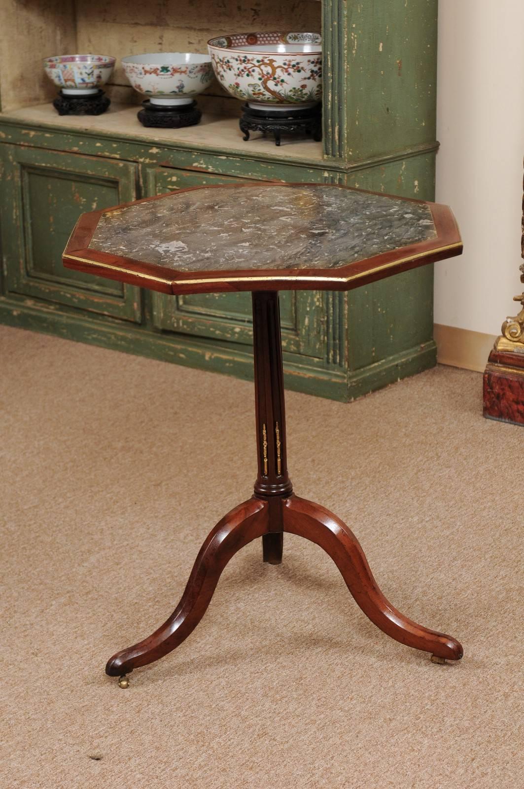 Mahogany tilt-top table on tripod base with brass banding, octagonal-shaped top with veneered gray marble.