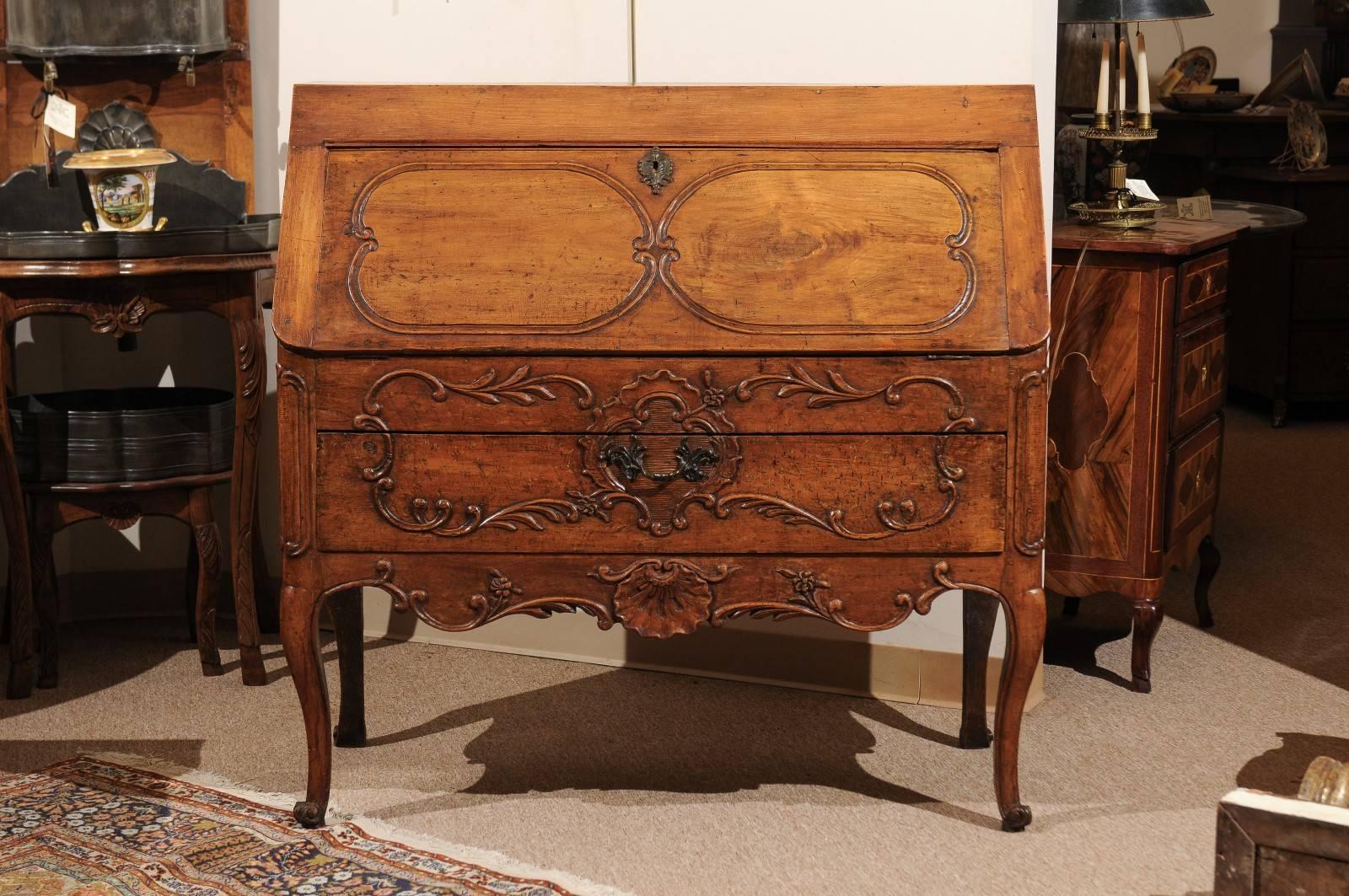 A French Regence fruitwood bureau slant front desk with fitted interior, shaped apron with shell carving ending cabriole legs.