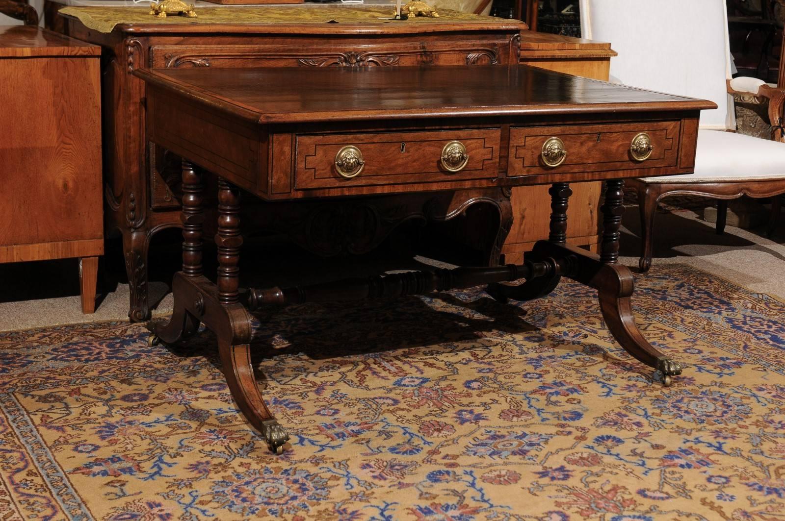 English Regency style mahogany writing table or desk with Greek key embossing on leather top, four drawers with lion head pulls, ebonized inlay, turned stretcher and splayed legs with brass paw castors. 

William Word Fine Antiques: Atlanta's