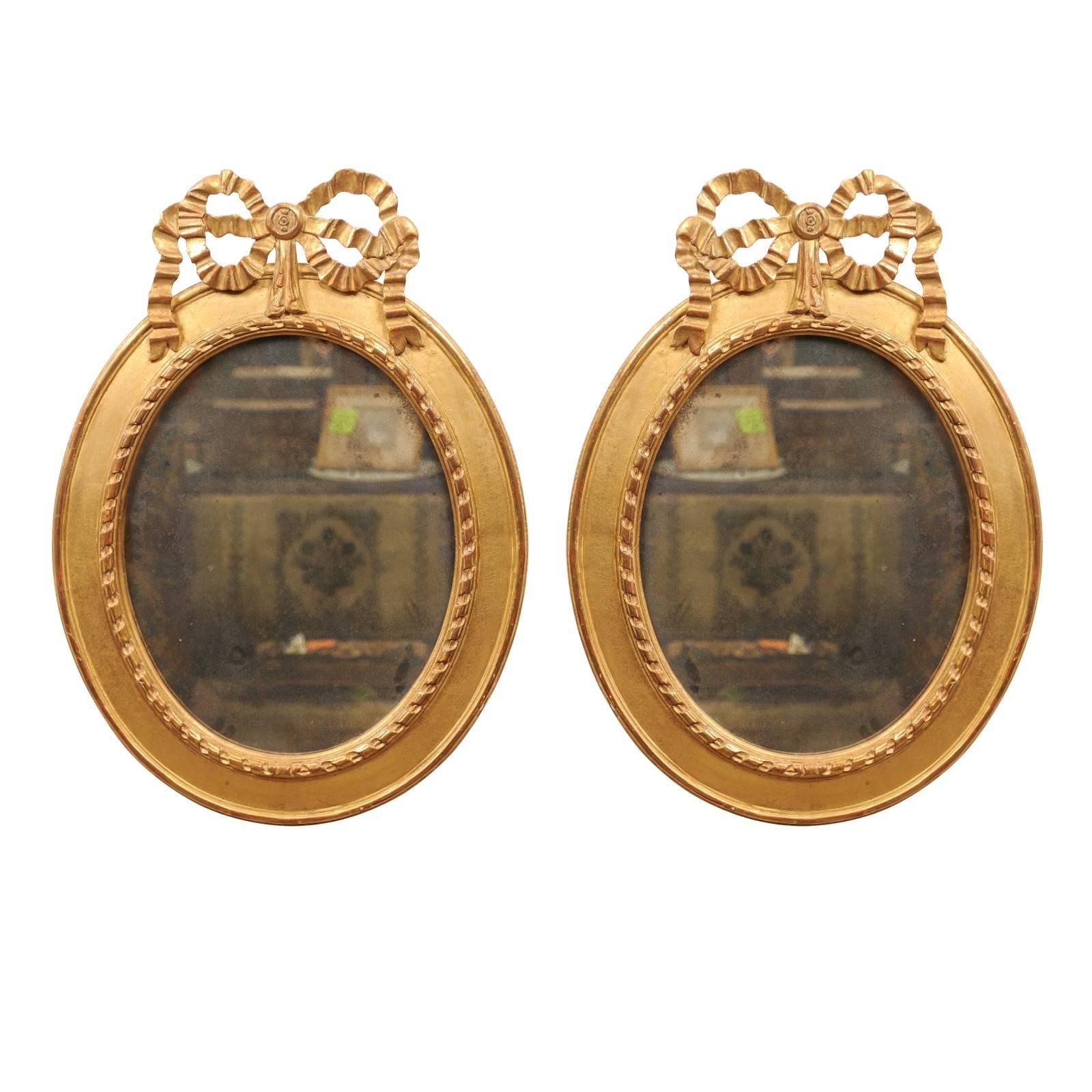 Paire de miroirs ovales en bois doré surmontés d'un nœud, 20ème siècle en vente
