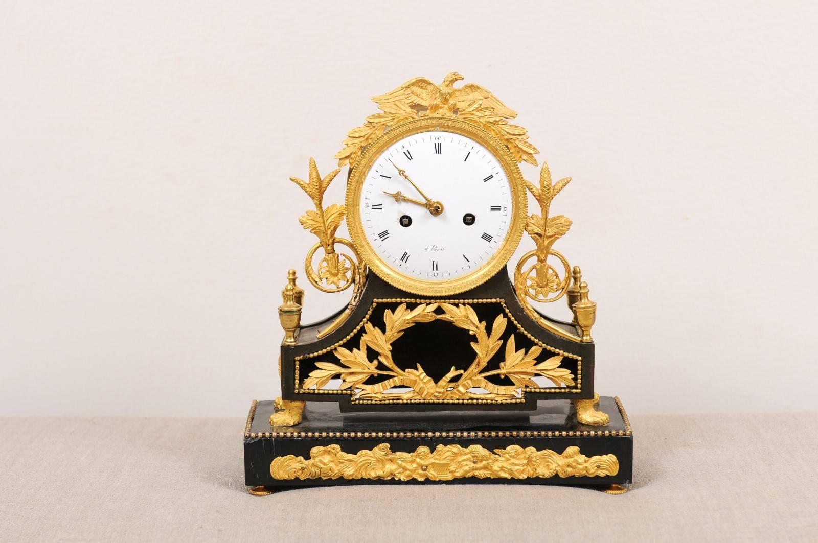 French Empire bronze doré mantel clock with an eagle crest resting on the circular clock face with white dial. Below is a two-tiered base with laurel wreath and paw feet and cherubs mounts. The rectangular base composed of black marble.

 