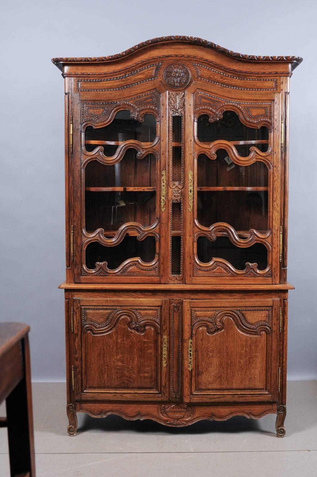 French Louis XV/XVI oak buffet deux corps/vitrine with carved arched cornice, glazed doors, shaped apron with urn carving detail and all resting on cabriole feet.