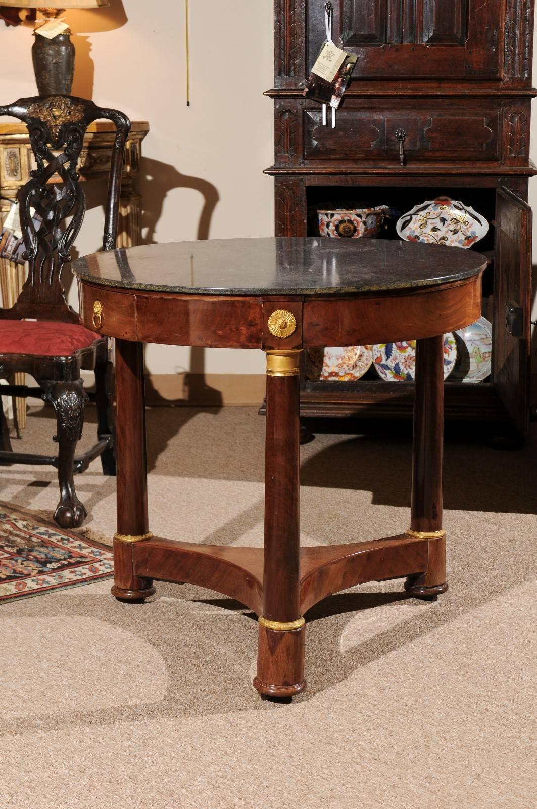 Empire Gueridon in mahogany with columns featuring gilt metal mounts, plinth base, and black marble top, France, circa 1810.