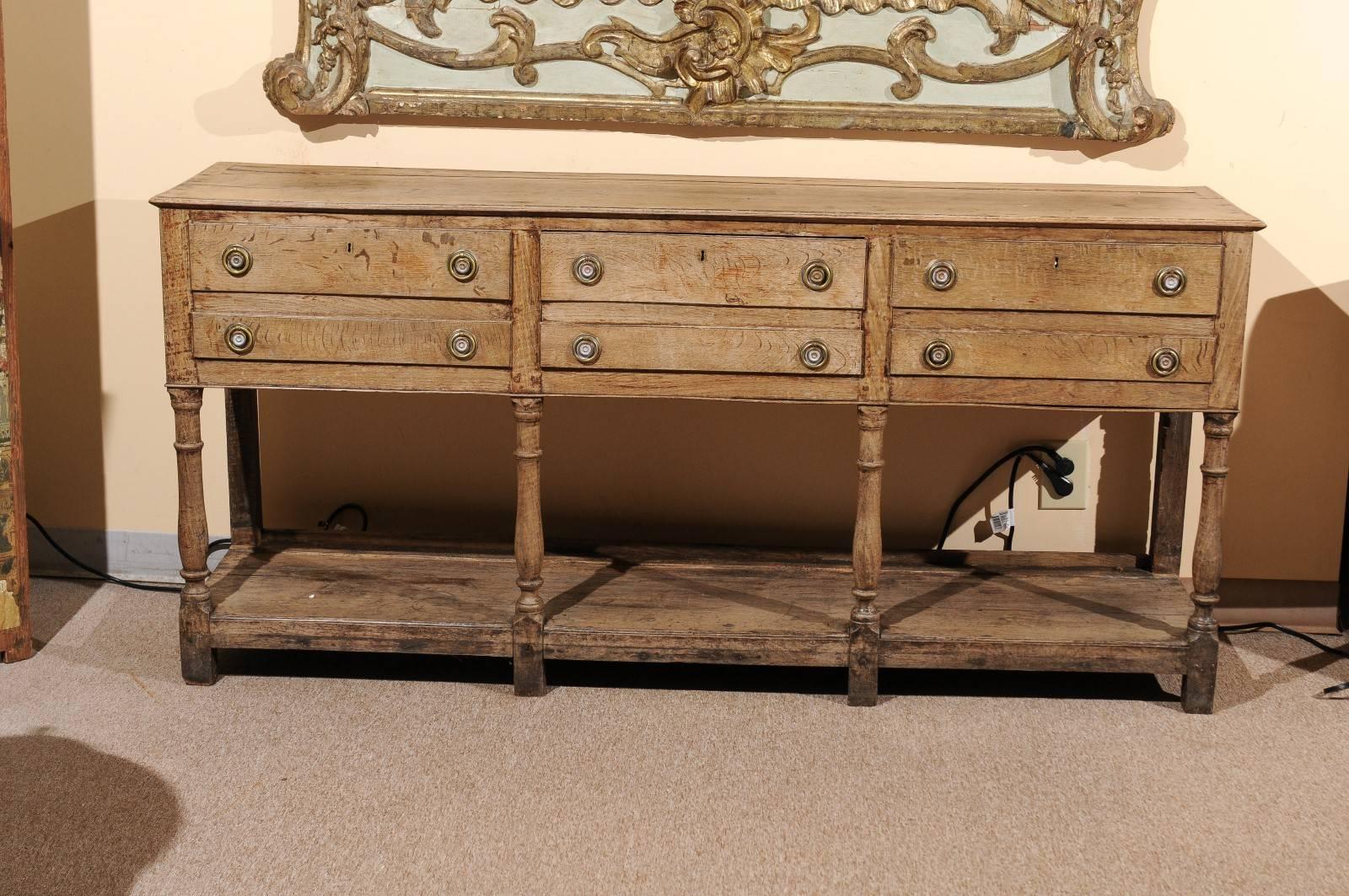 18th century English oak dresser base with lower plinth and turned legs in bleached finish. The piece has five drawers--a central deep drawer flanked by two shallow drawers flanking each side.