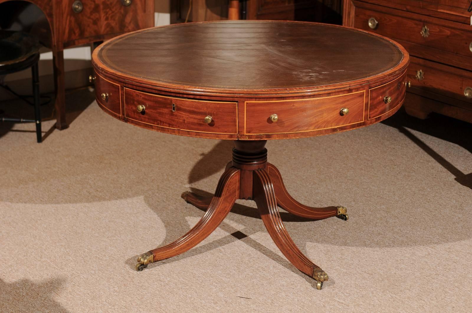 English Revolving 19th century rent table in mahogany and satin wood with brown embossed leather top, string inlay, four drawers, splayed reeded legs and brass paw castors. 

William Word Fine Antiques: Atlanta's source for antique interiors since