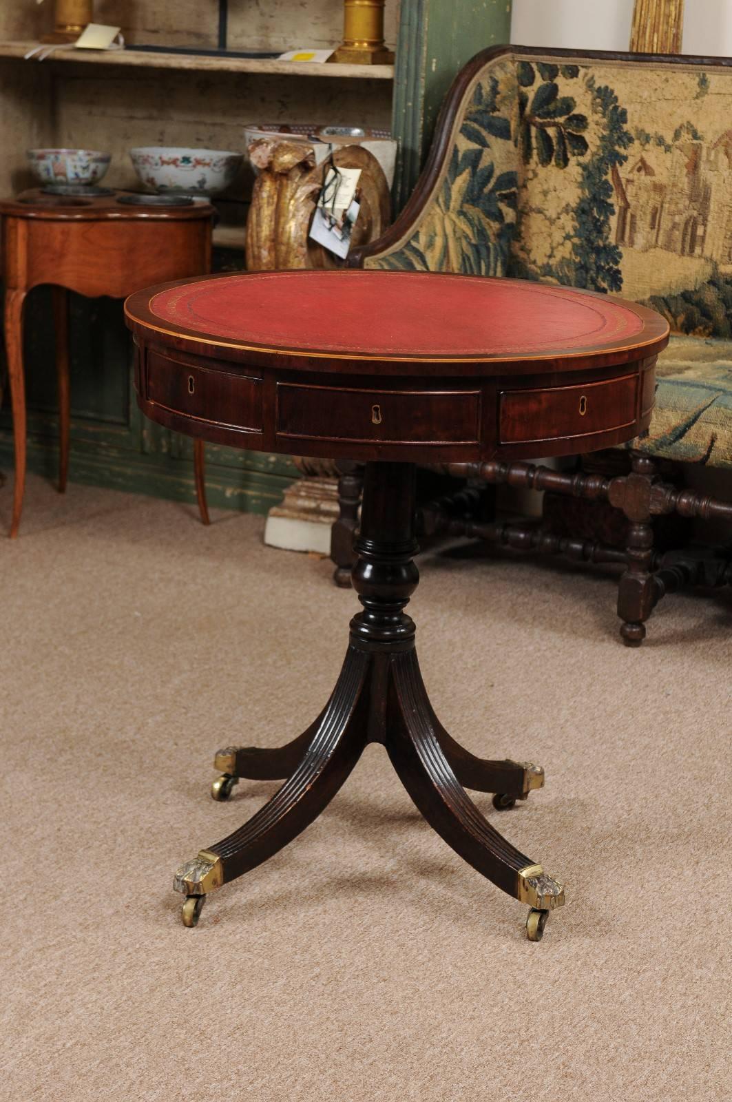 Revolving English Regency drum table in mahogany with embossed red leather top, four drawers and reeded splayed legs with brass paw castors. 

William Word Fine Antiques: Atlanta's source for antique interiors since 1956.
  