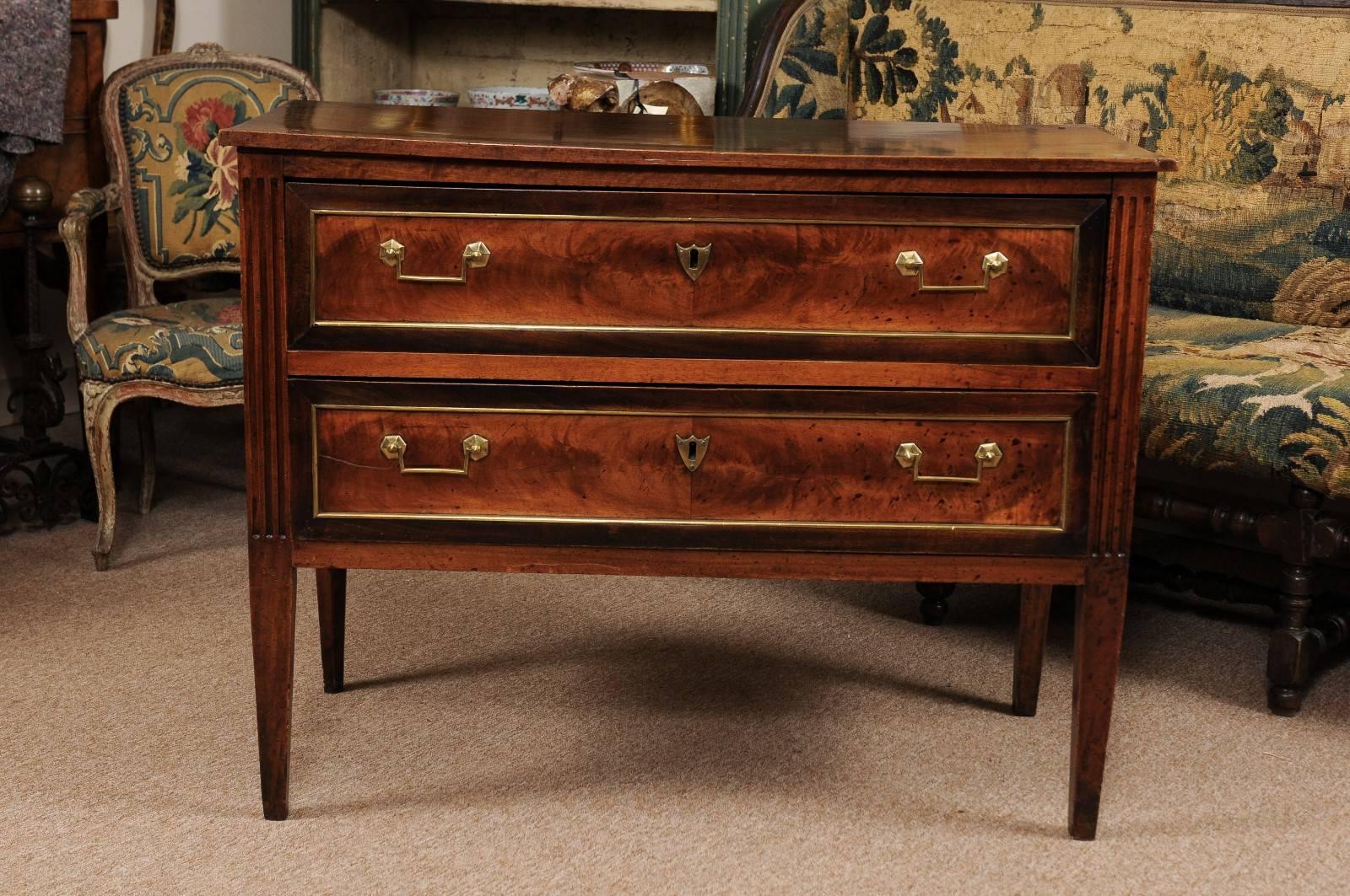 The XVI French commode in walnut with rich patina, carved fluted detail, two drawers with brass pulls and trim. All resting on tapered legs.