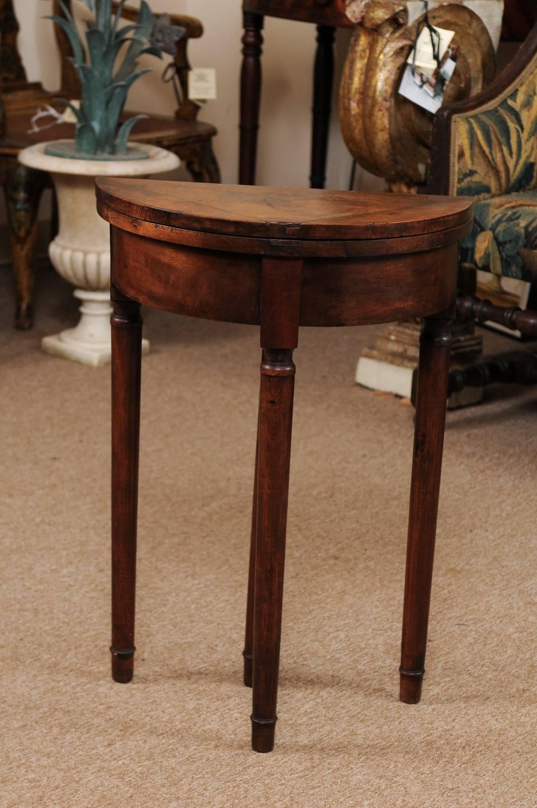 Petite walnut demilune side table with tapering legs; converts to round game table via drawer mechanism with hidden chip compartment, late 19th century, Italy.