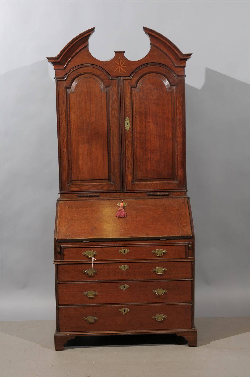 A George I oak bureau bookcase with broken pediment, blind doors with enclosed fitted interior, and the bureau with enclosed fitted interior, writing surface and four drawers below. All resting on bracket feet. 

   