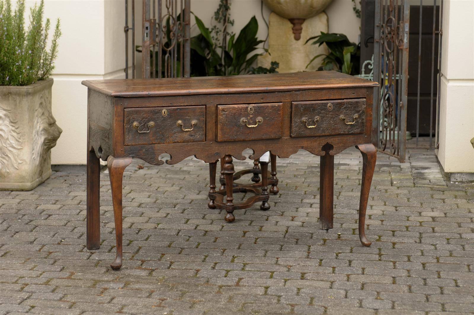 This English oak server from the late 18th century features a three-plank rectangular top with beveled edge over three drawers. The central smaller drawer is flanked with two larger ones adorned with two bail handles and central escutcheons, placed