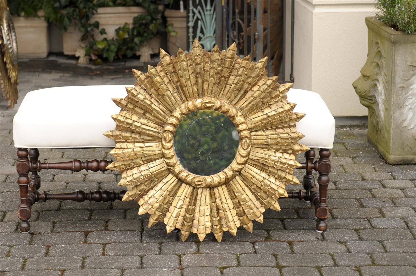 This large size French giltwood sunburst mirror from the mid century features a round mirror surrounded by a raised carved molding. The sunburst part is made of an array of sunrays of varying sizes. The ensemble is in great condition, the mirror has