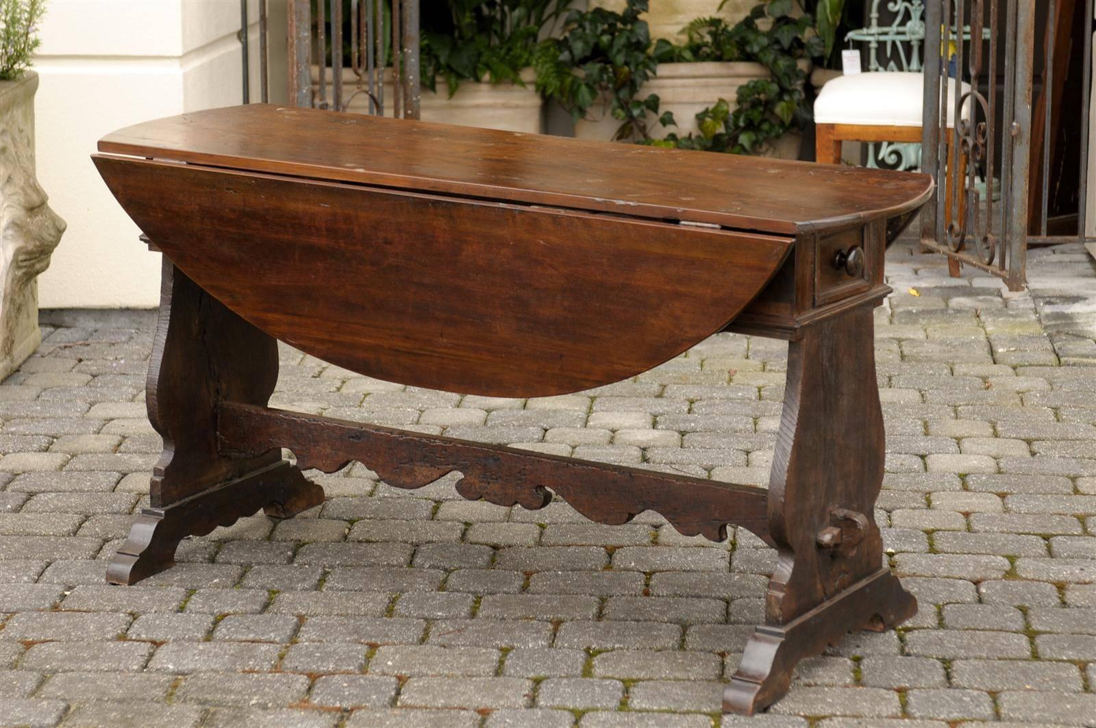Oval 18th century Italian walnut drop-leaf table. This Italian table features an oval drop-leaf top. The top sits on a trestle base adorned with a nicely carved cross stretcher.  Each leaf is 12.5 inches, giving this table a depth of 30.25 inches
