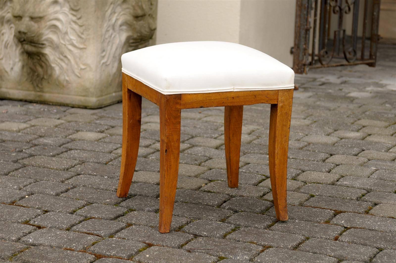 This French Biedermeier style stool features a square seat with new muslin upholstery. The neutral color of the upholstery allows the warmth of the four saber legs and simple skirt to shine. The simplicity of the lines and the richness of the wood