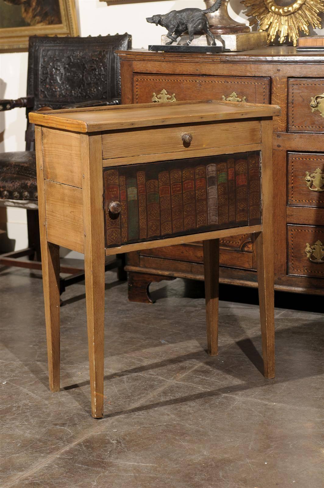 An English side table with drawer and faux book door from the late 1800s. This uncommon English side table in pine features a rectangular top on a belt with one drawer and a cupboard with a painted faux book door. The structure rests on four
