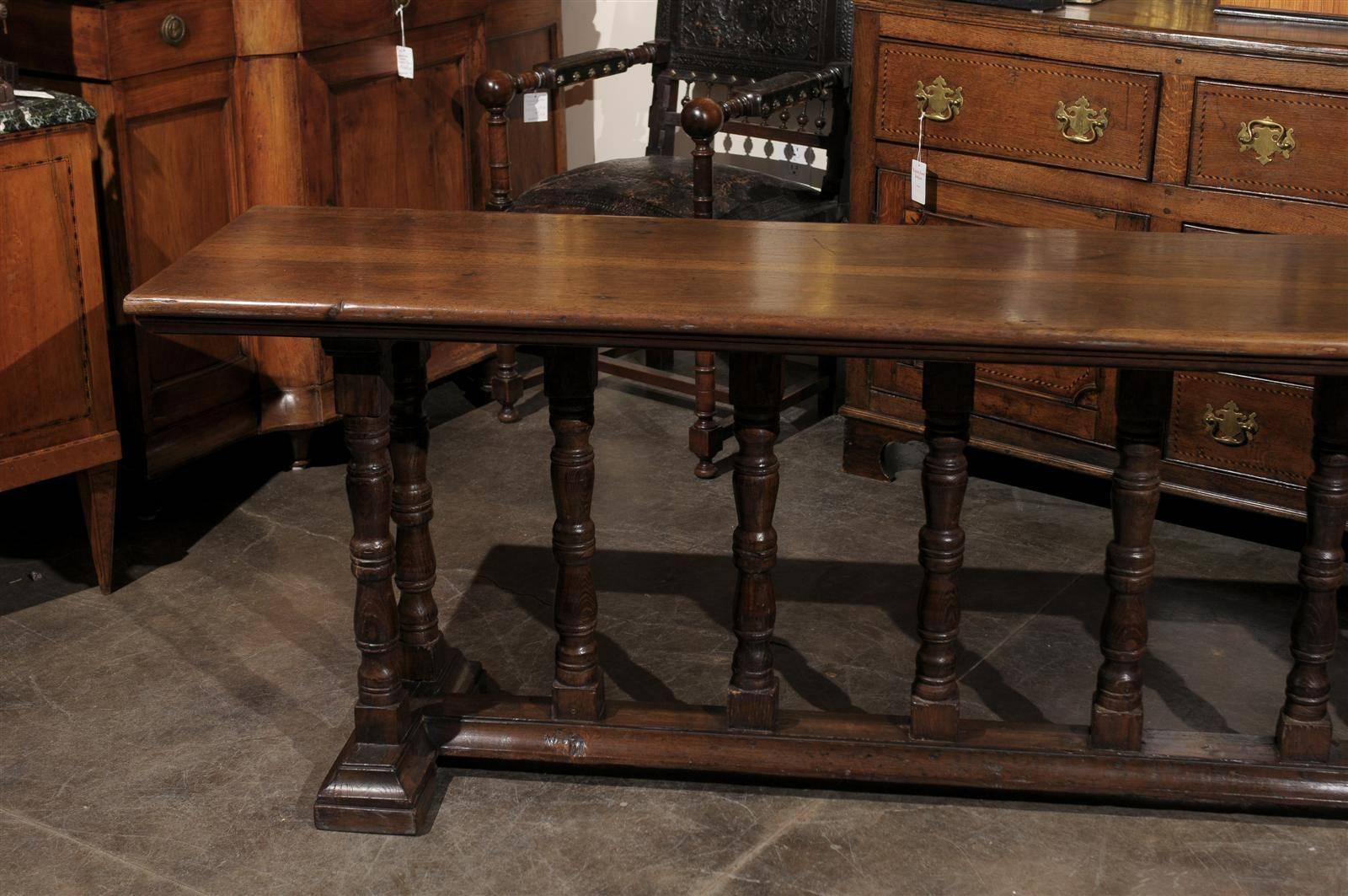 This Italian walnut long side or console table from the early 19th century features a narrow rectangular top over and unusual trestle base. The turned legs, placed on each side of the table, are rhythmically repeated along the cross stretcher. No