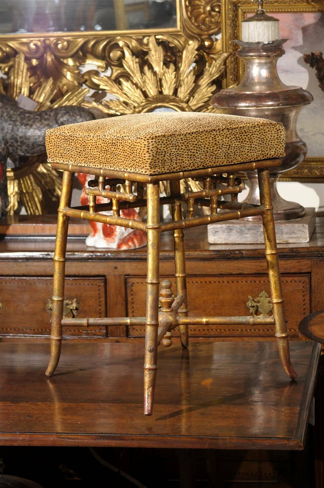 This Italian vintage gilt iron stool from the mid 20th century features a square seat upholstered with faux animal print upholstery. The skirt is adorned with motifs reminiscent of the Chinese Chippendale style. The gilded iron faux-bamboo frame is