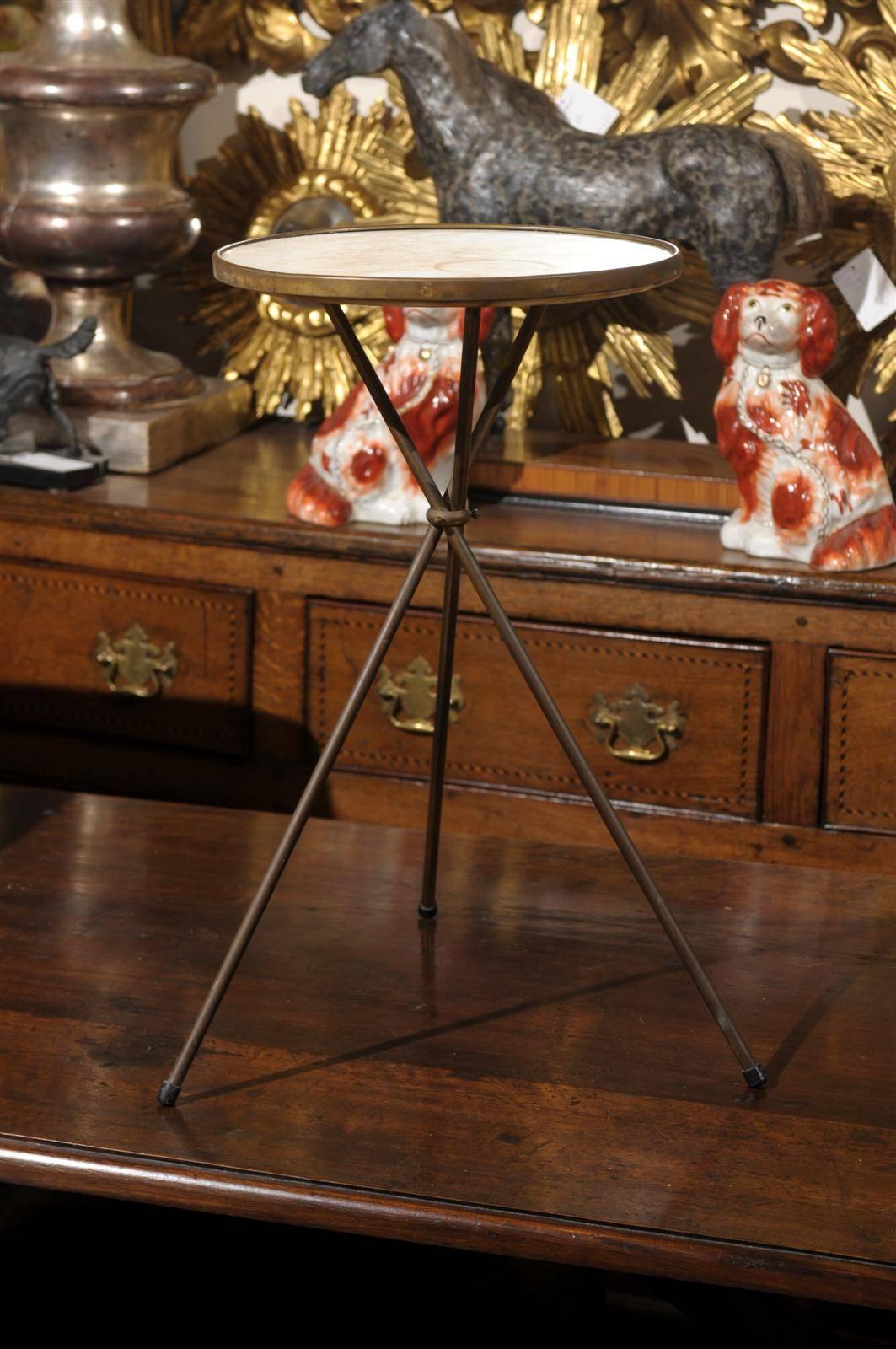 This slender French drinks table from the mid-20th century features a round marble top of cream color over an unpolished brass three legged base. A circular link braces the three legs mid-way, giving a certain elegance and stability to this modern