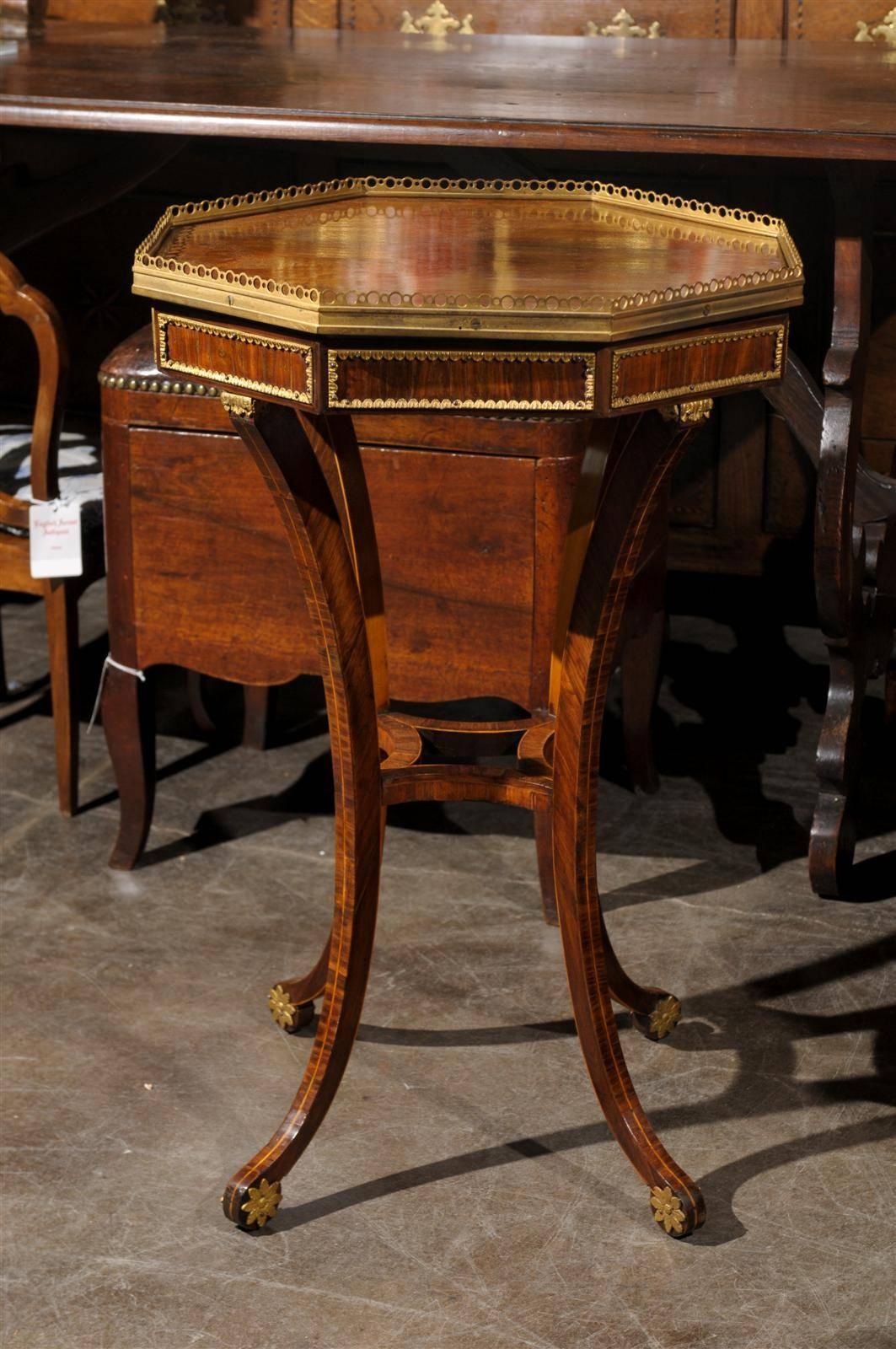 This English Regency rosewood veneered side table from the mid 19th century features an exquisite octagonal top surrounded by a brass gallery. The brass décor is repeated in the apron, nicely framing each panel of the octagon. The four splayed legs