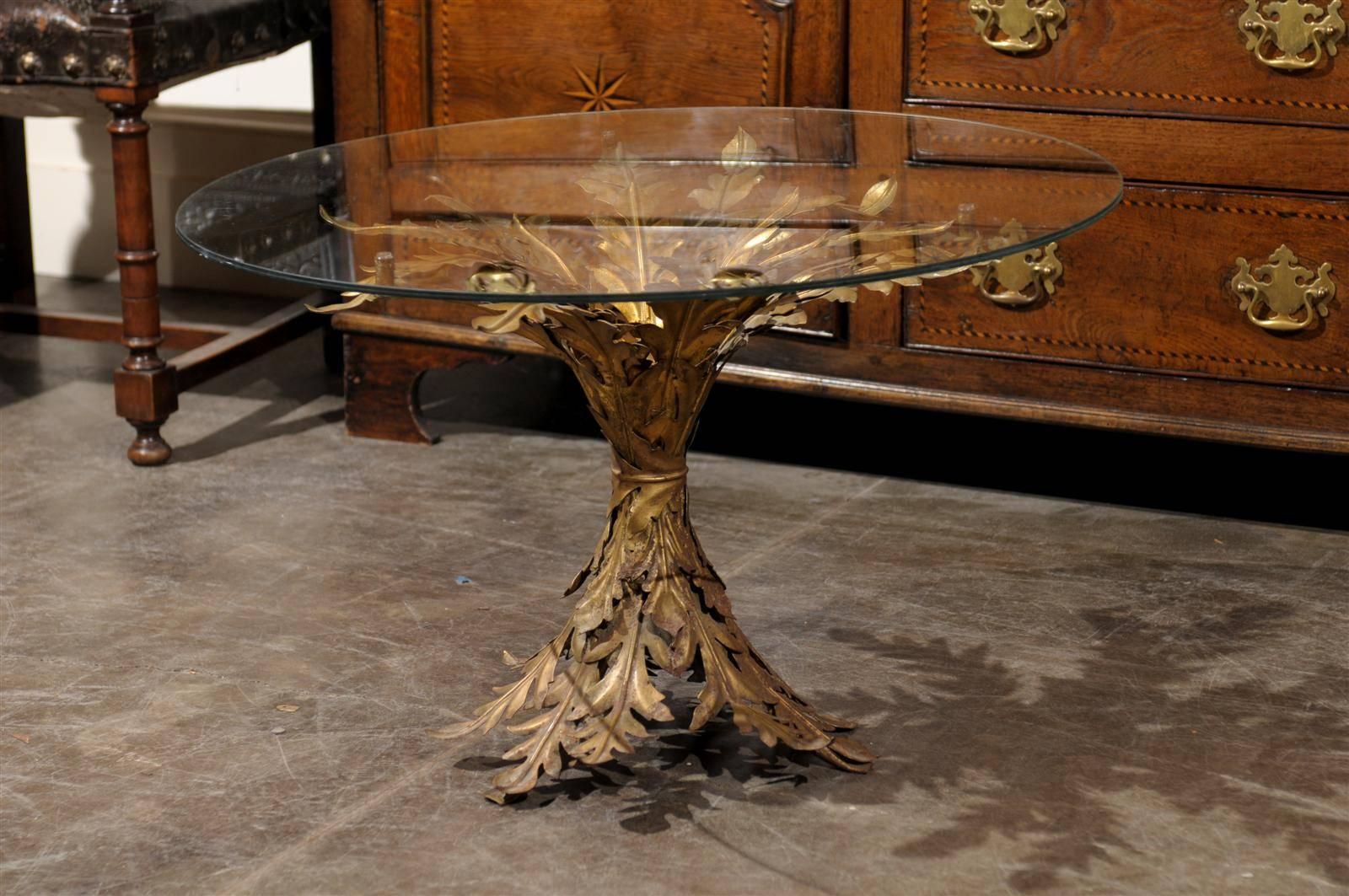 A vintage Italian gilt metal pedestal table with glass top. The base of this Italian gilt metal table is entirely decorated with a foliage motif that expands at the bottom, draws narrow in the middle and blossoms at the top. The top of this circa