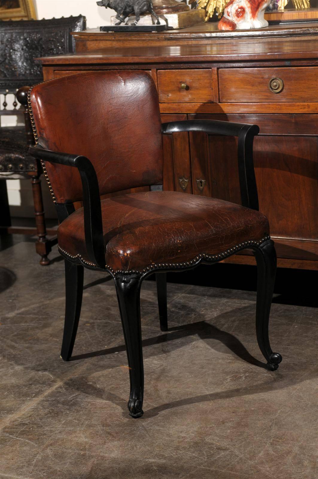 This pair of French Art Deco armchairs from the early 20th century features their original brown leather backs and seats over an ebonized wood structure. The backs, decorated with nail head trims, are slightly curved, allowing the sitter to rest his