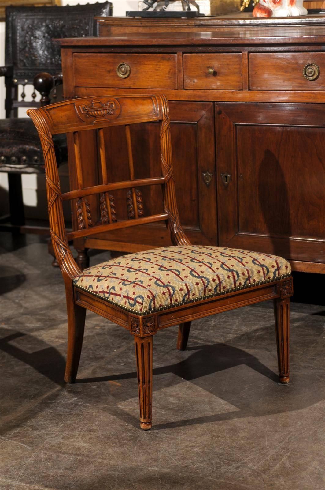 A French carved back slipper chair with needlepoint seat circa 1920-1930.  This elegant French slipper chair features a carved back which recalls the theme of the hunt with motifs of quivers and arrows.  The top rail of the back is adorned with a