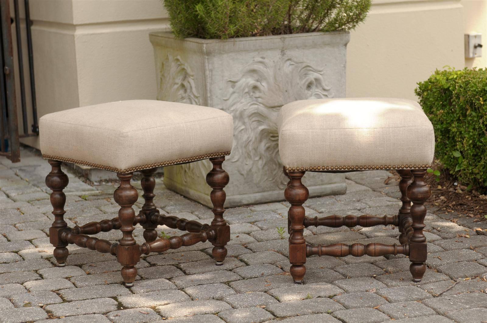 A pair of English walnut stools from the mid 19th century. Topped with square seats upholstered in muslin with nail head trims, each stool is raised on four beautifully wooden turned feet with block joints connected to one another with turned